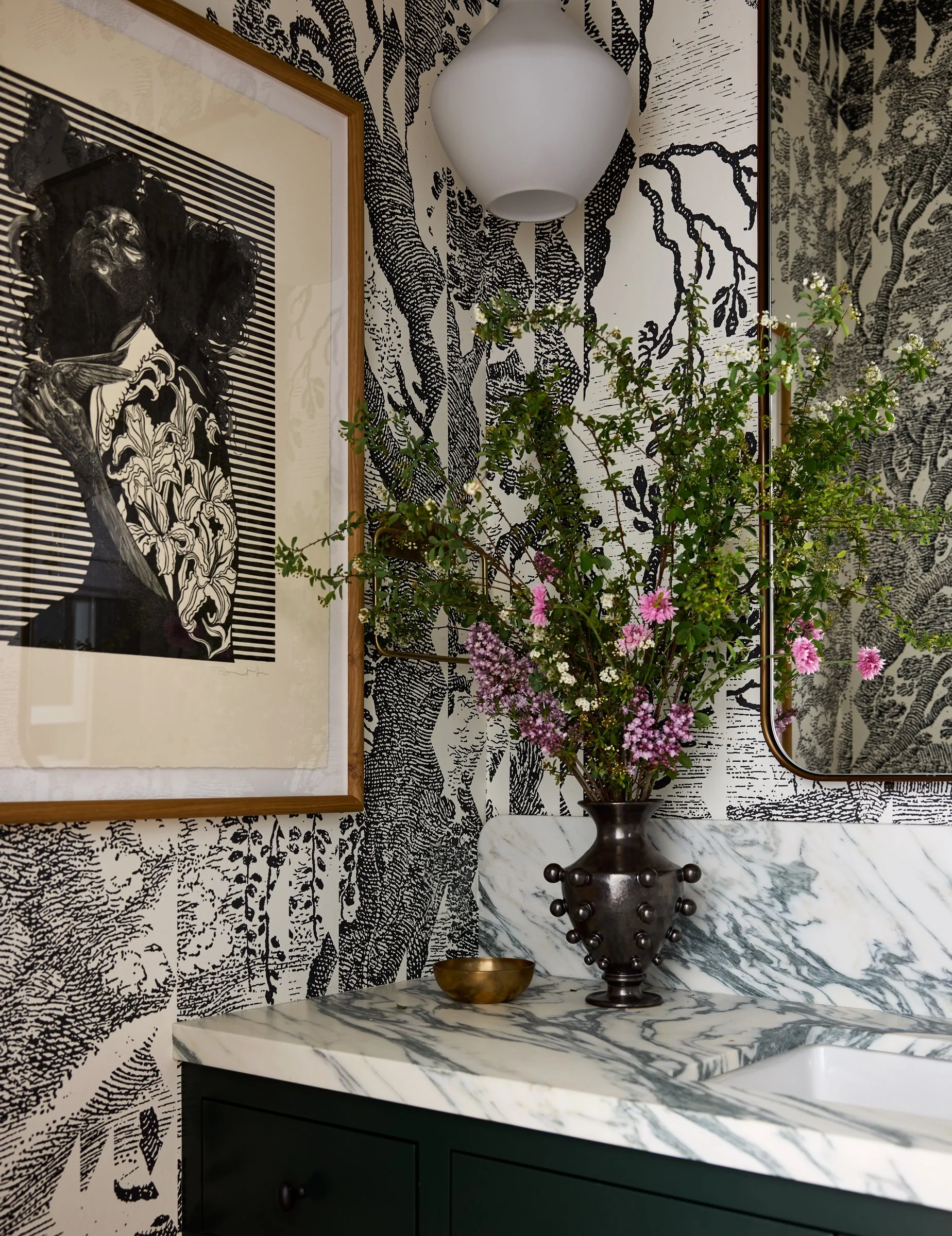 Powder room with bold black-and-white botanical wallpaper, a marble vanity counter, dark green cabinet, and framed art