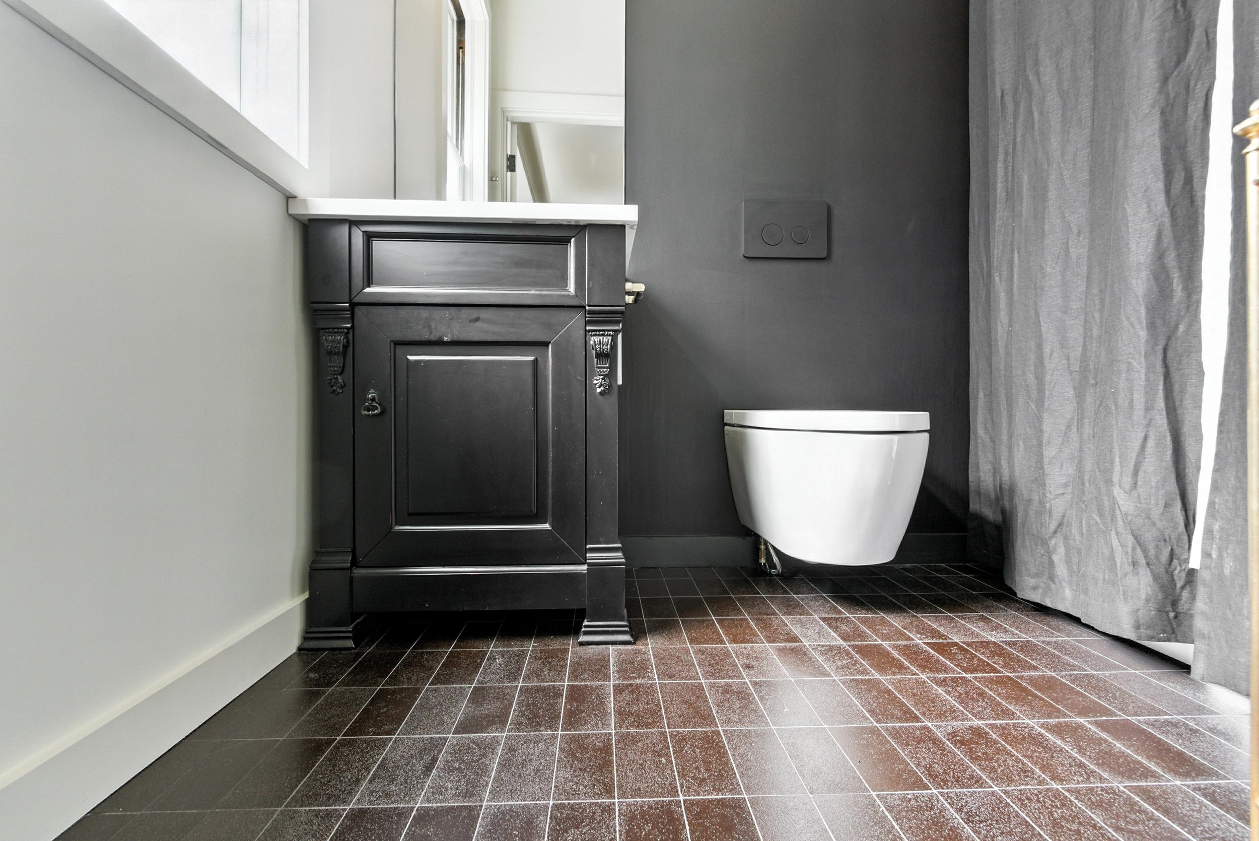 Bathroom with black vanity cabinet, wall-mounted toilet, gray walls, and terracotta tile floor