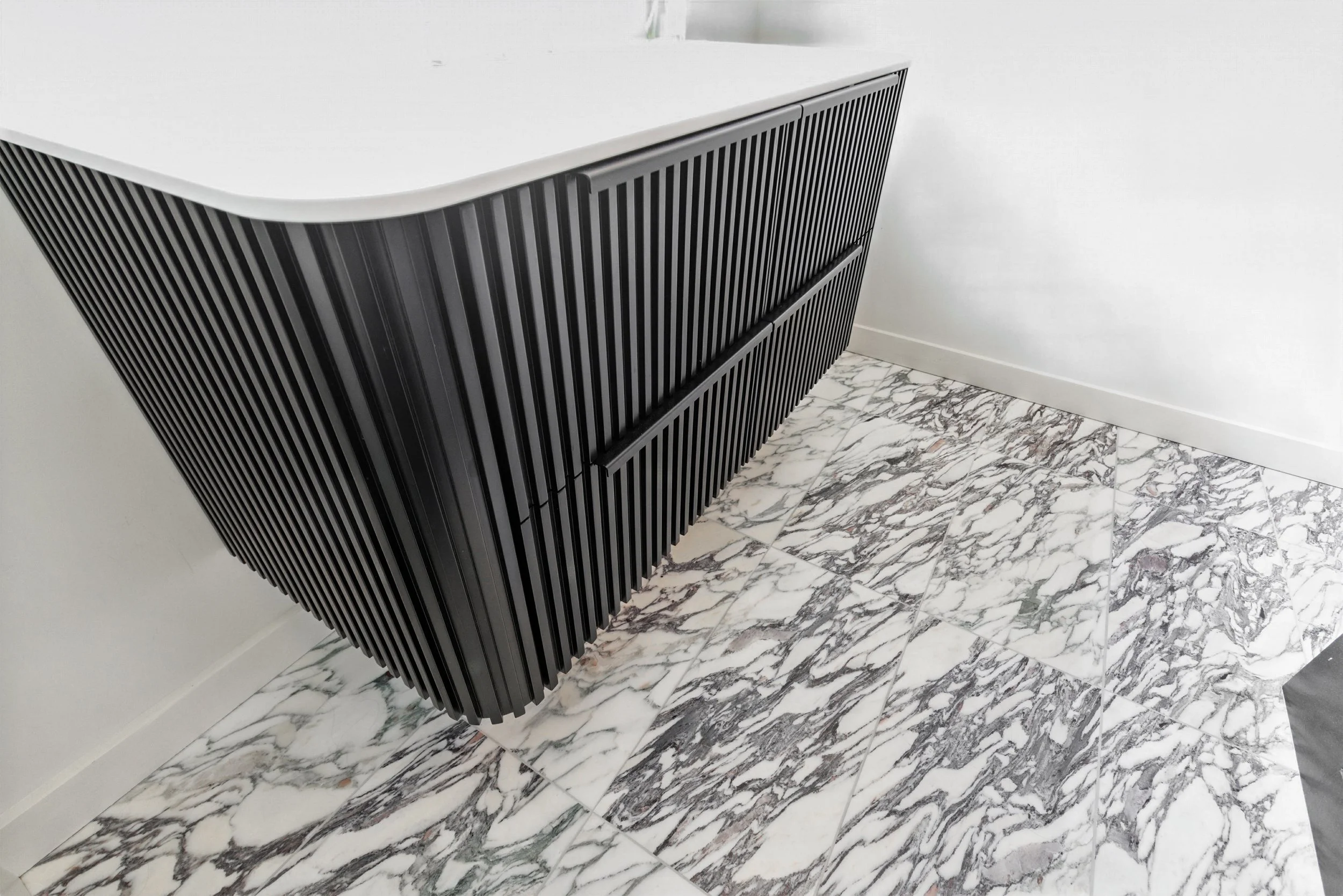 Floating black fluted vanity with white countertop over white and gray marble tile flooring