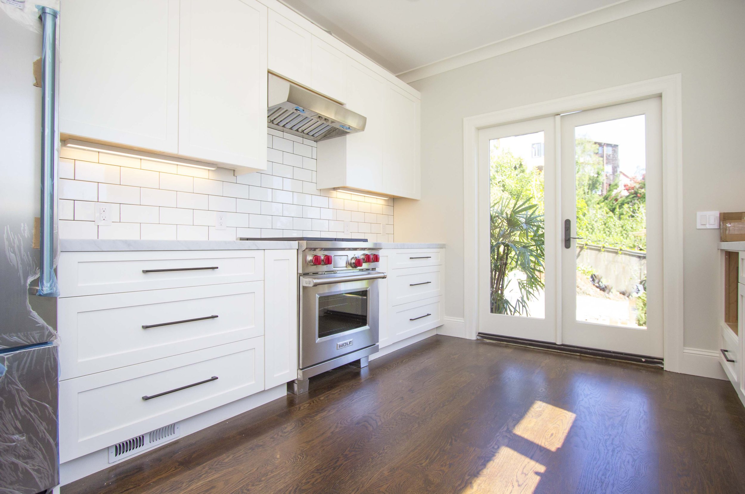 White kitchen with a subway tile backsplash, a stainless range and hood, hardwood floors, and glass doors to the outside