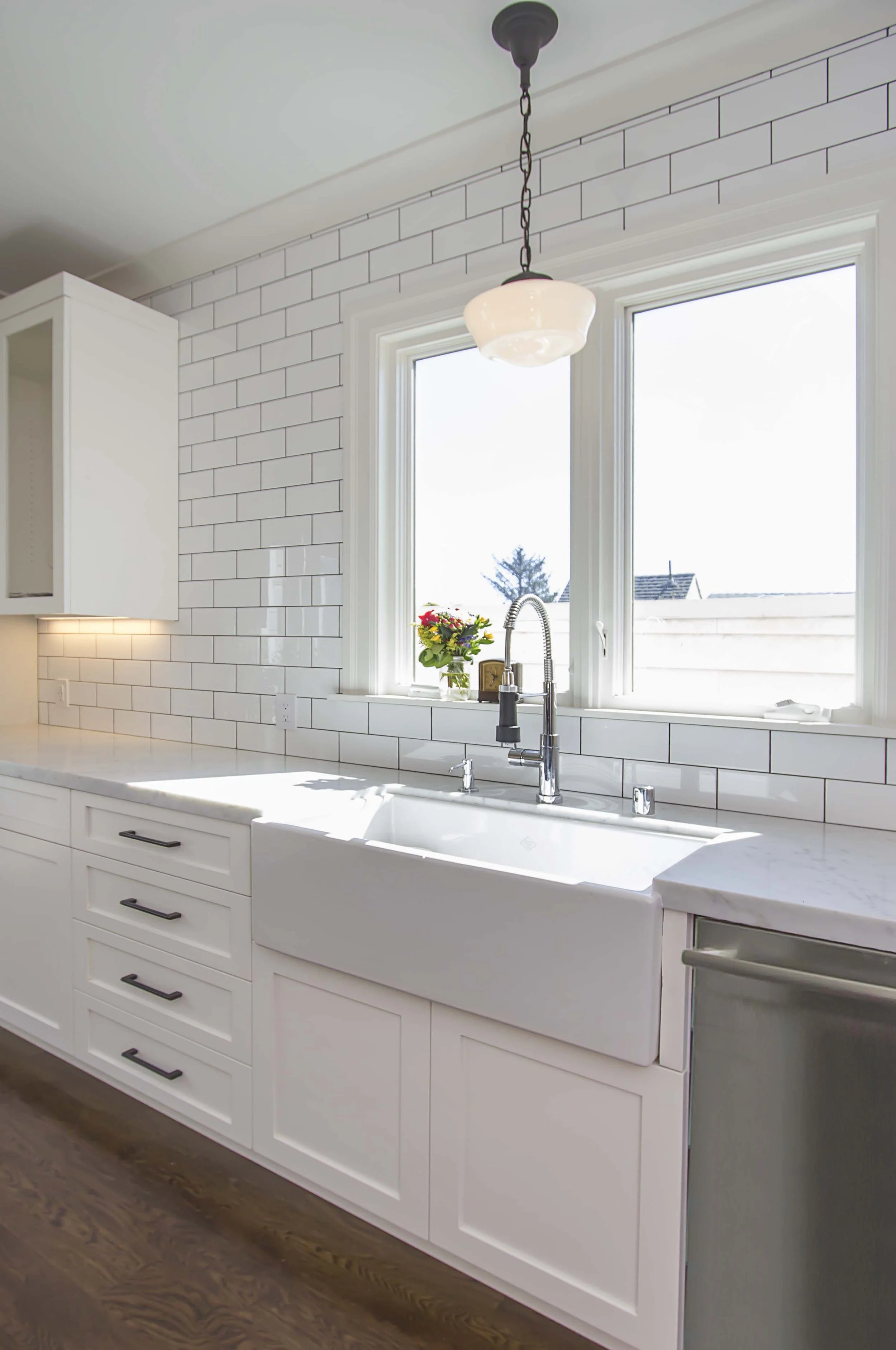 White kitchen with a farmhouse sink, a brass faucet, a subway tile backsplash, and a window with a view