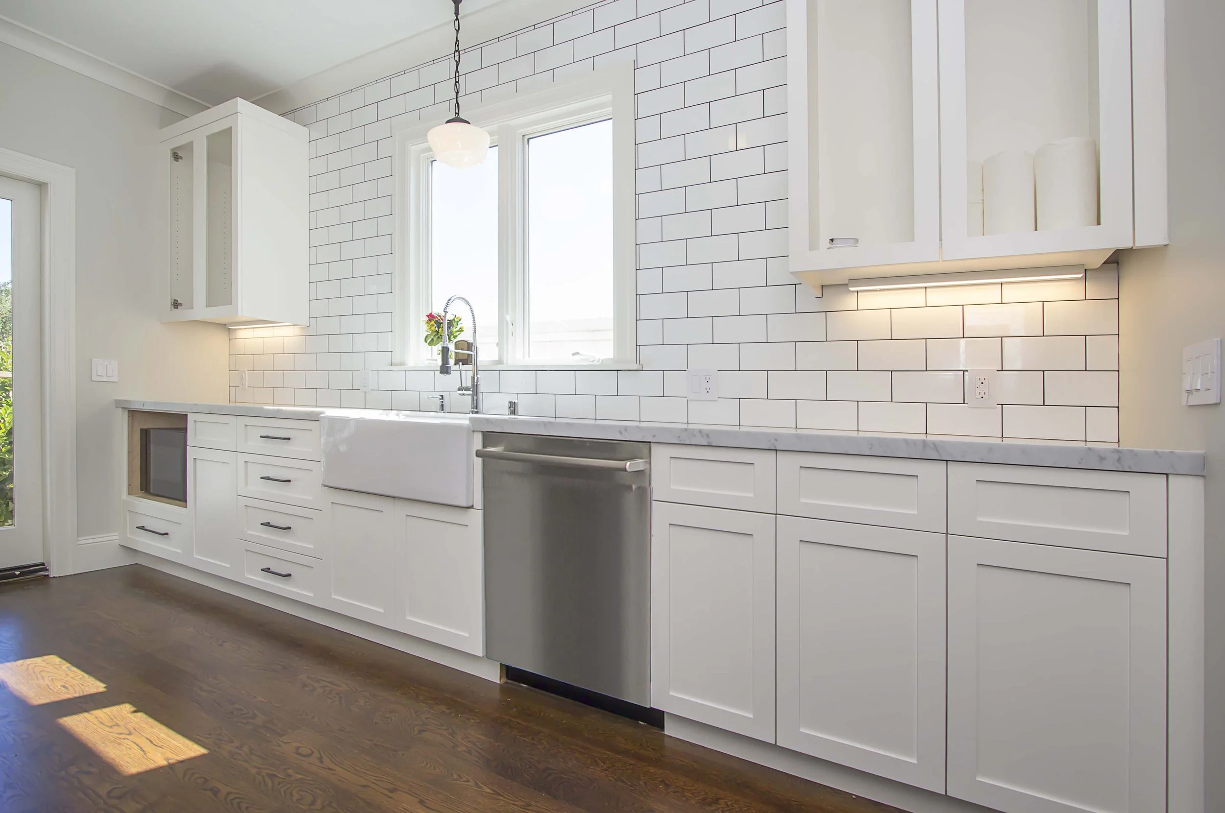 White kitchen with a farmhouse sink, a stainless dishwasher, a subway tile backsplash, and hardwood floors