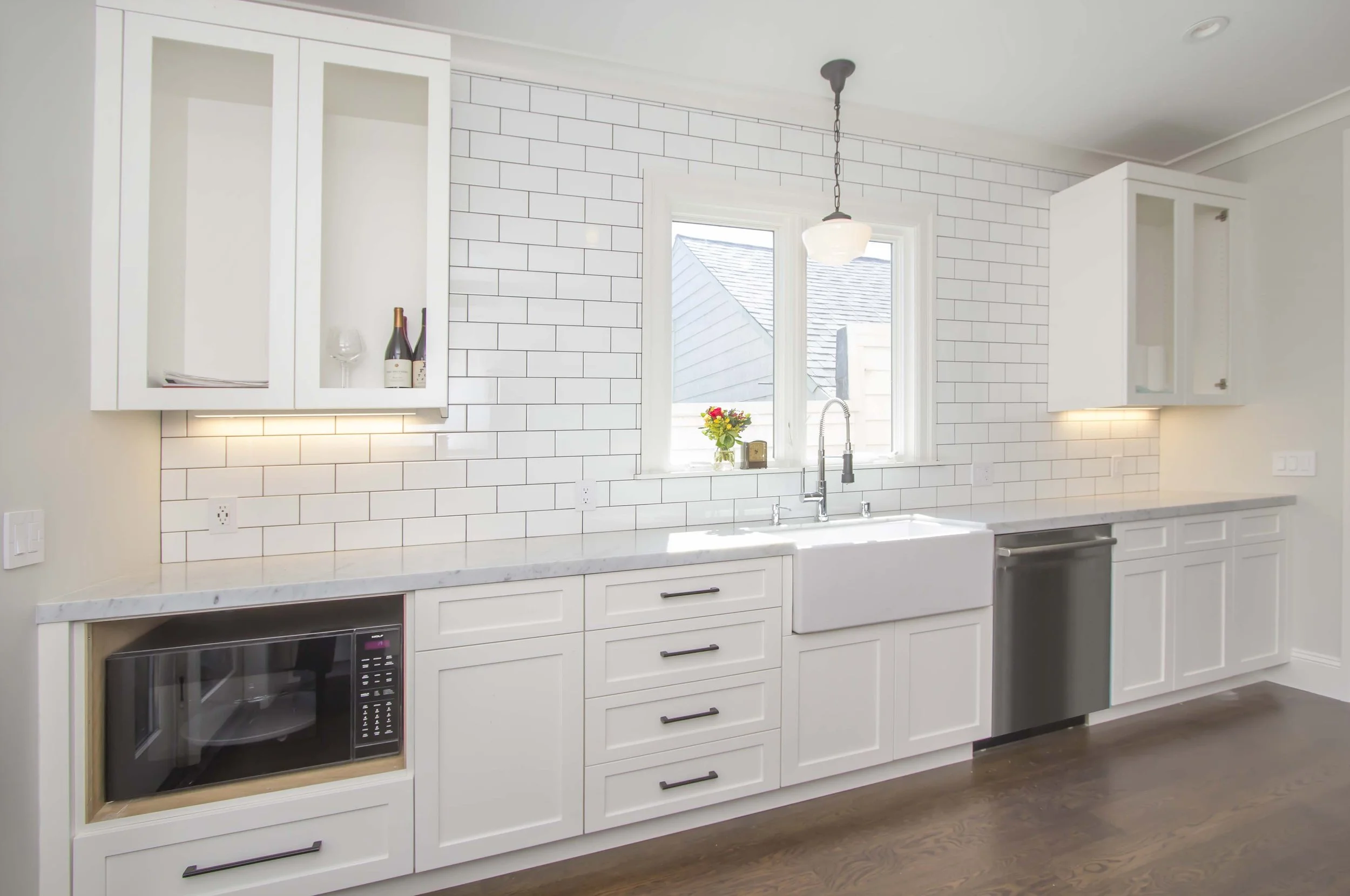 White kitchen with a farmhouse sink, a built-in microwave, a subway tile backsplash, and a window
