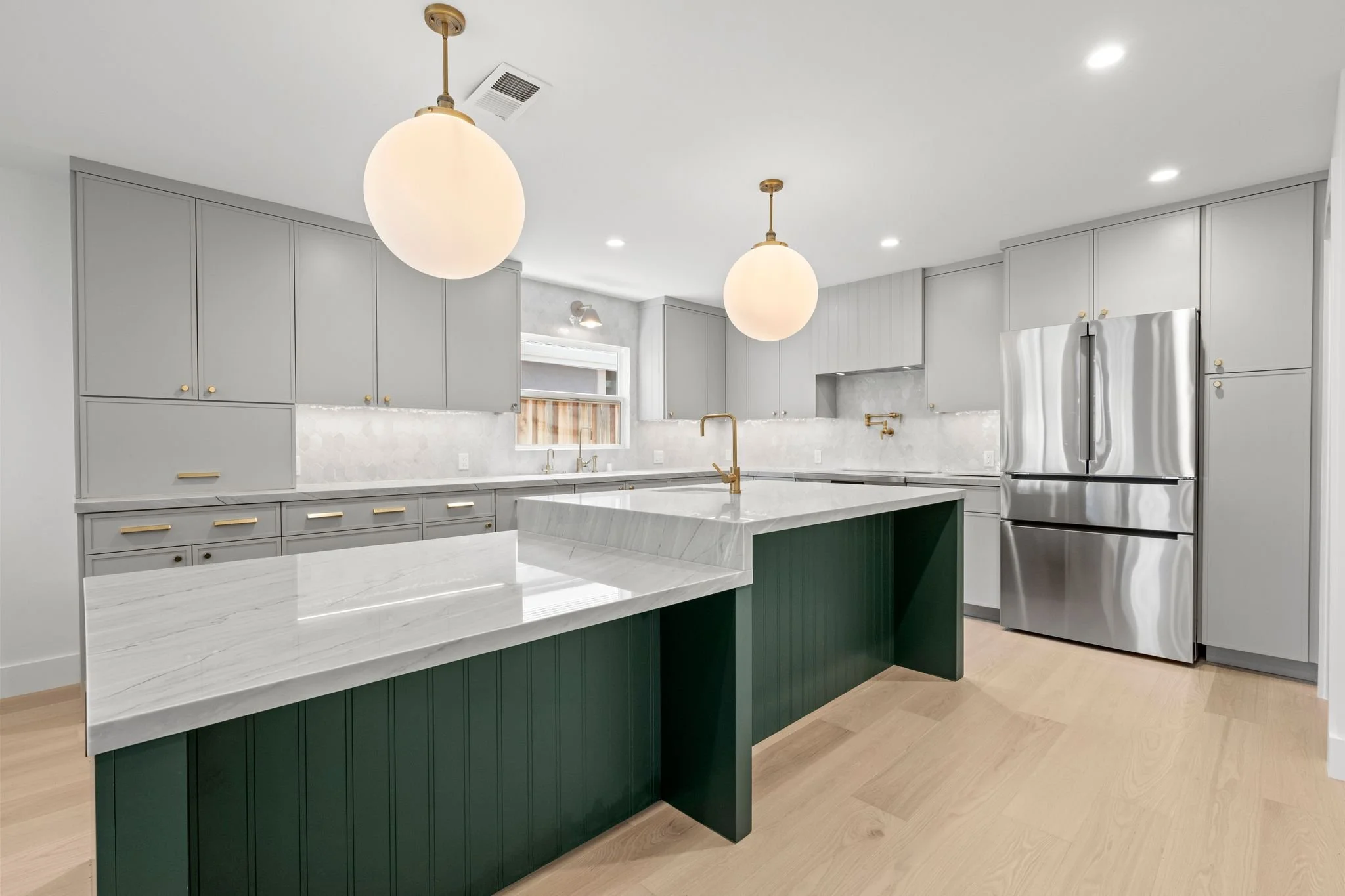 Kitchen with a green island, a white waterfall countertop, globe pendant lights, gray cabinets, and a stainless refrigerator