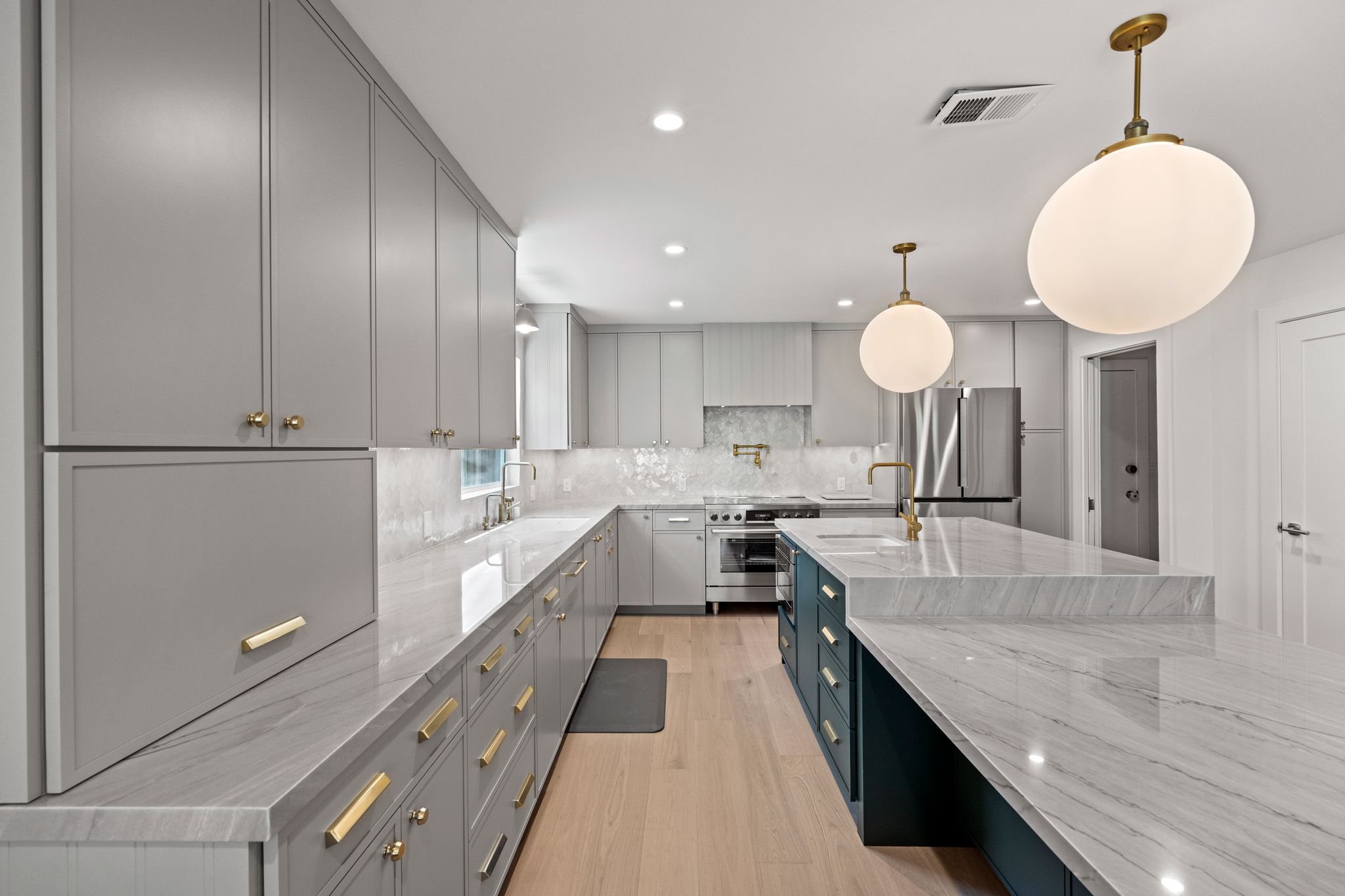 Kitchen with gray cabinets, marble countertops, globe pendant lights, brass hardware, and light hardwood floors