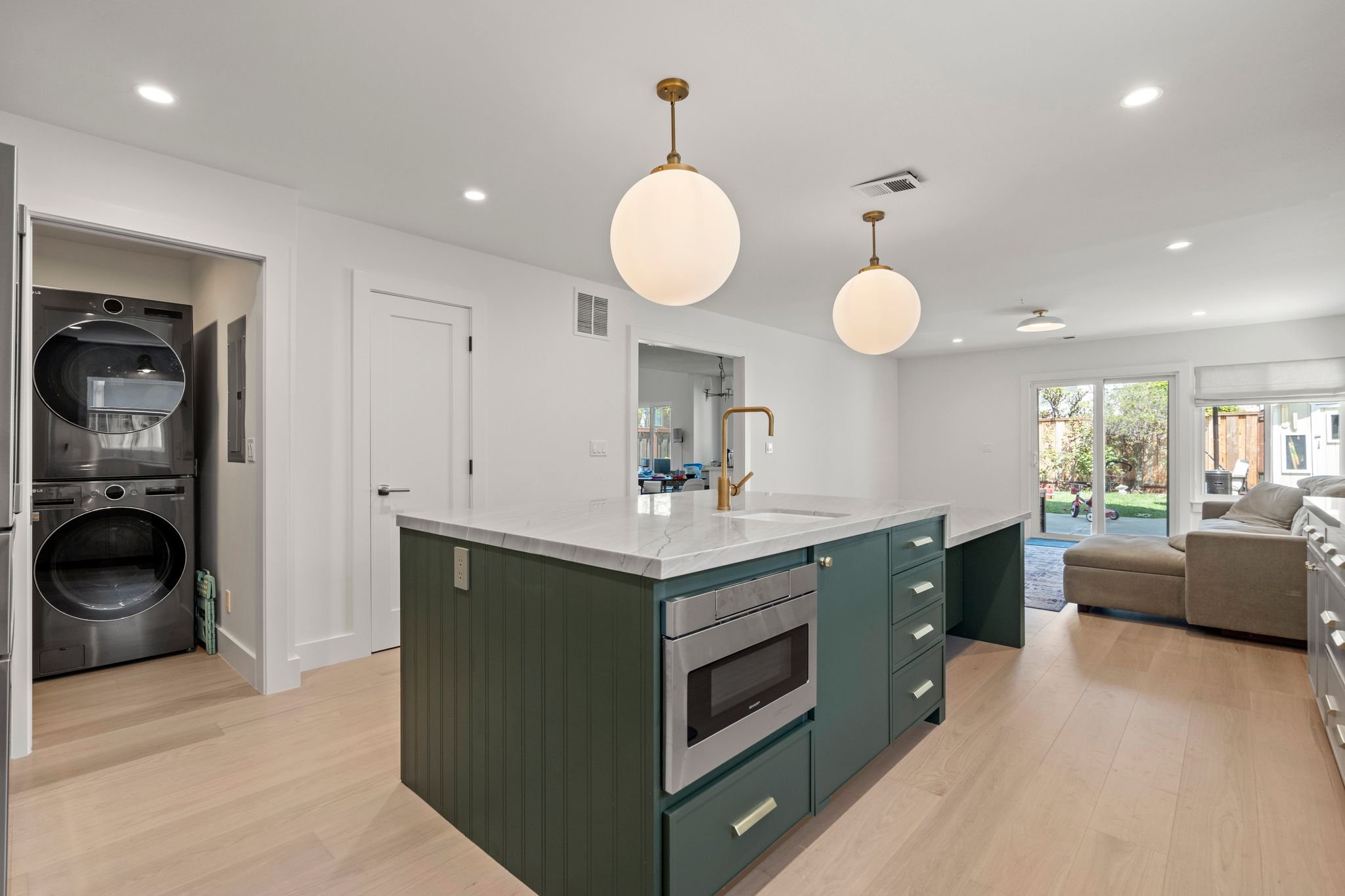 Kitchen with a green island, globe pendant lights, a stacked washer and dryer, and an open living area beyond