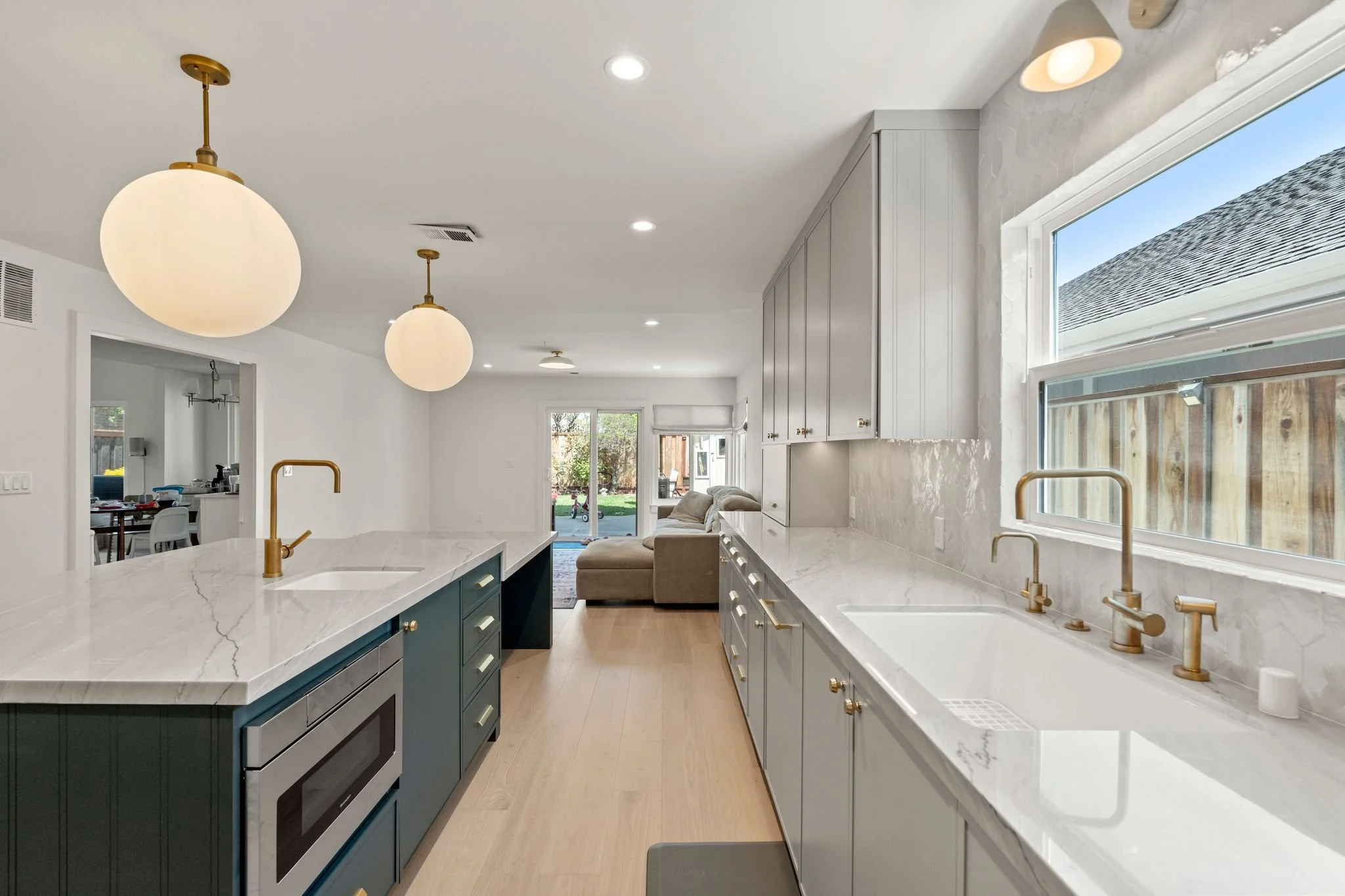 Kitchen with a green island, a brass faucet, globe pendant lights, and a window overlooking a fenced yard