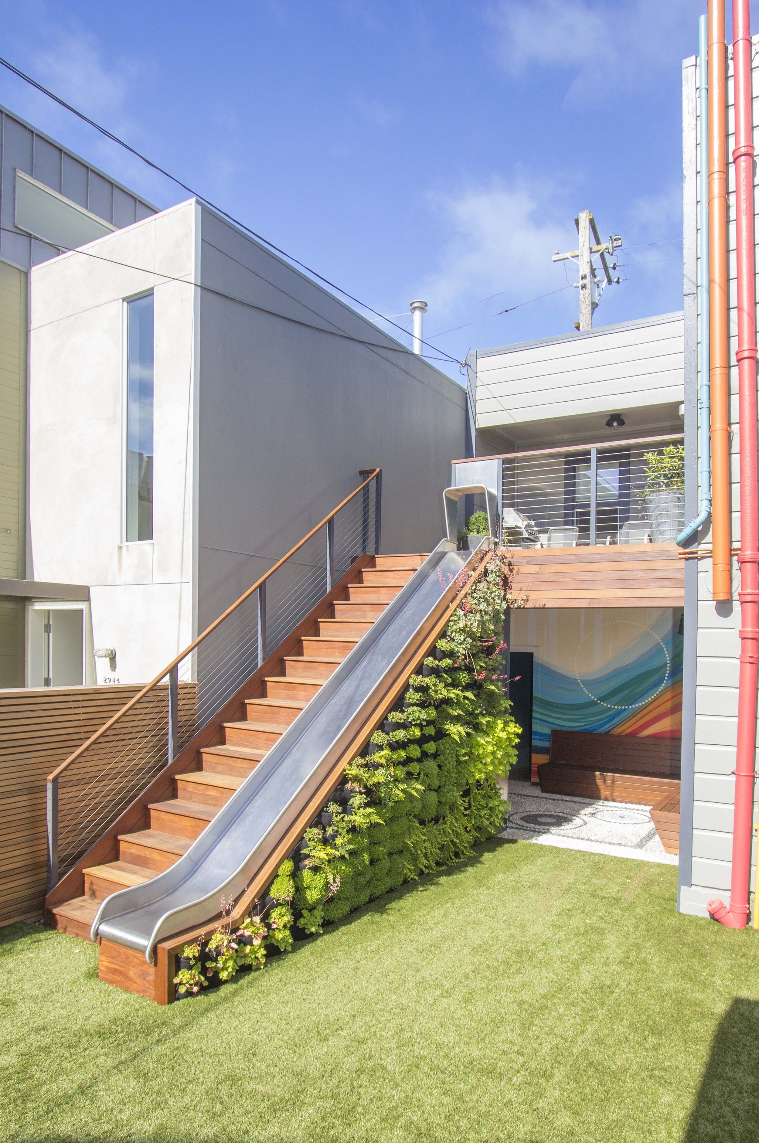 Backyard with an artificial turf lawn, wood steps with a metal railing, and a green living wall