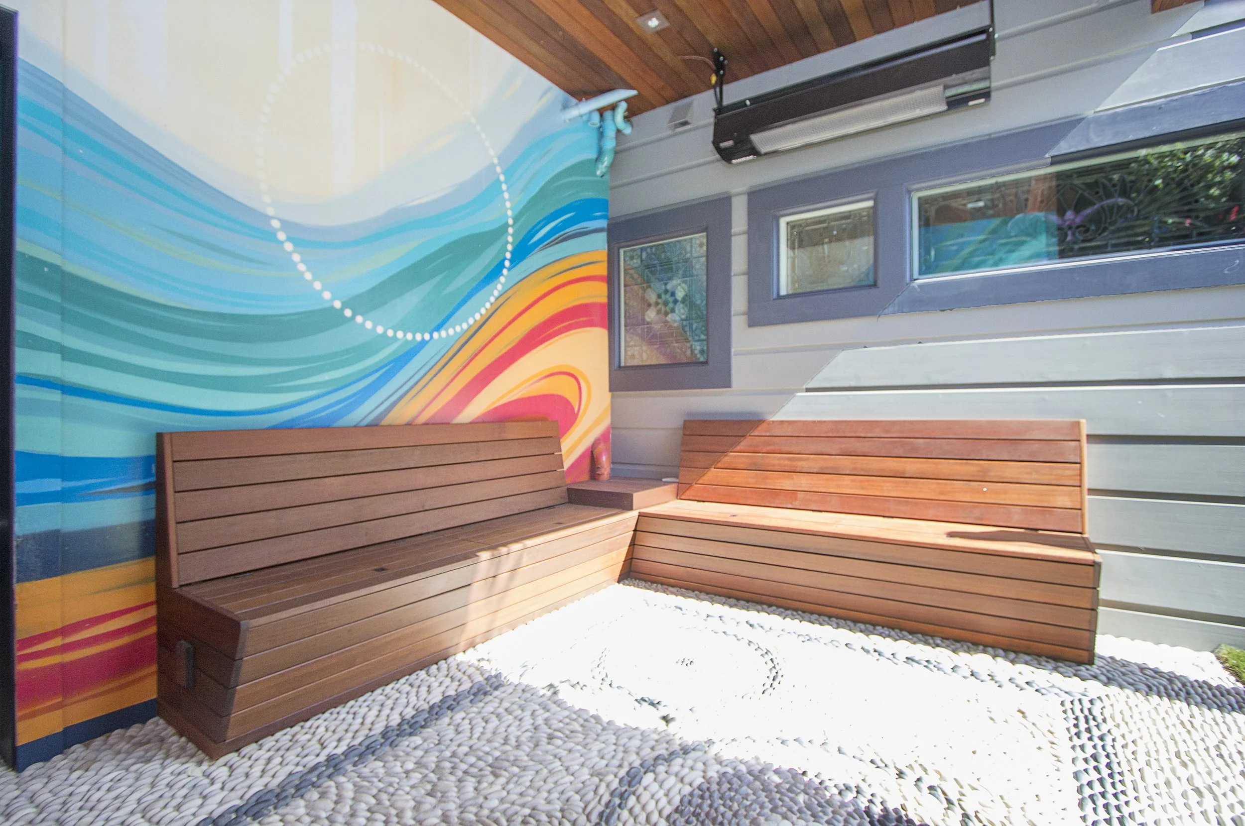 Covered patio with ipe wood bench seating in front of a colorful abstract wall mural