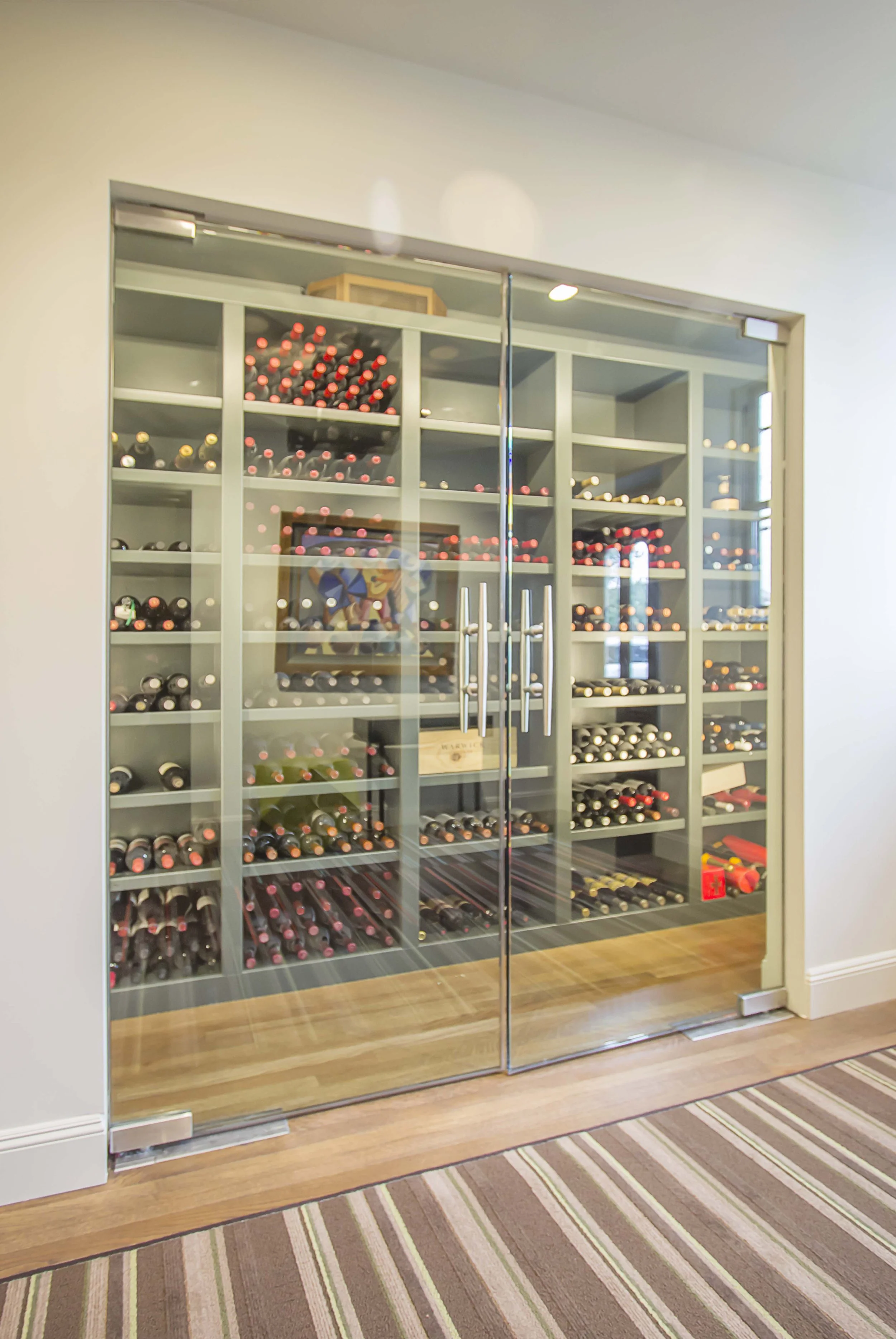 Glass-door wine cabinet stocked with wine bottles, set against a striped floor