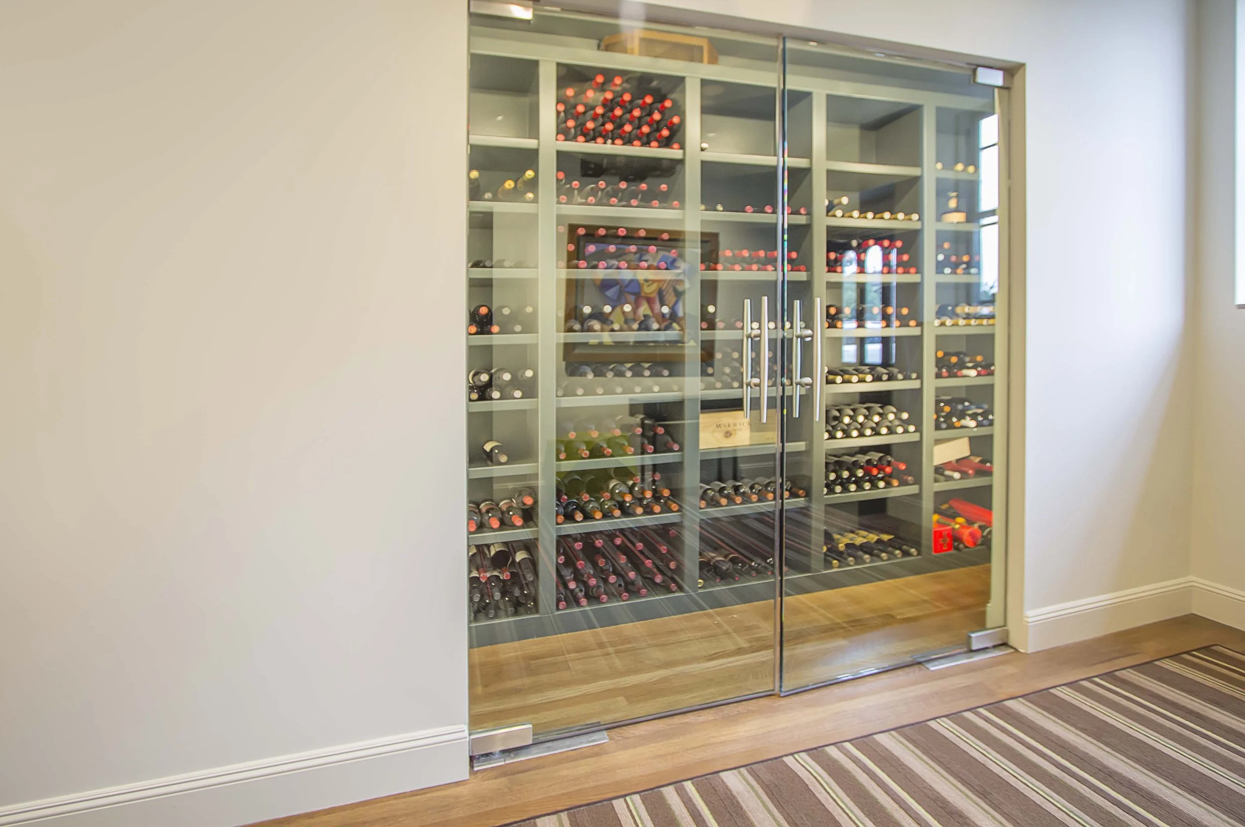 Large glass-enclosed wine cellar built into a wall with backlit shelves of wine bottles