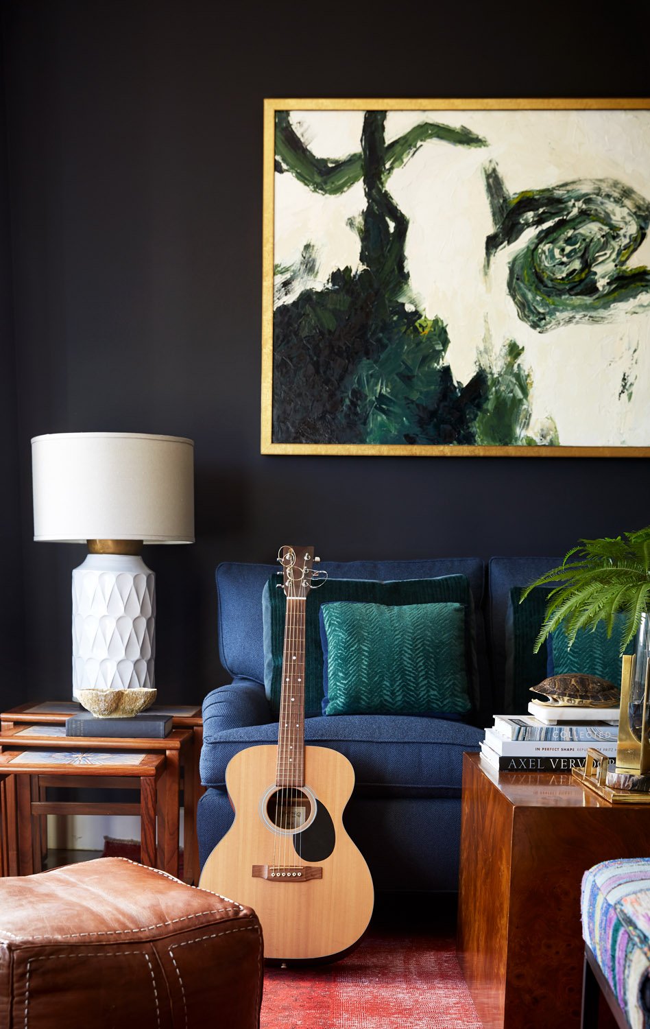 Corner sitting area with a dark accent wall, abstract artwork, a white table lamp, and an acoustic guitar
