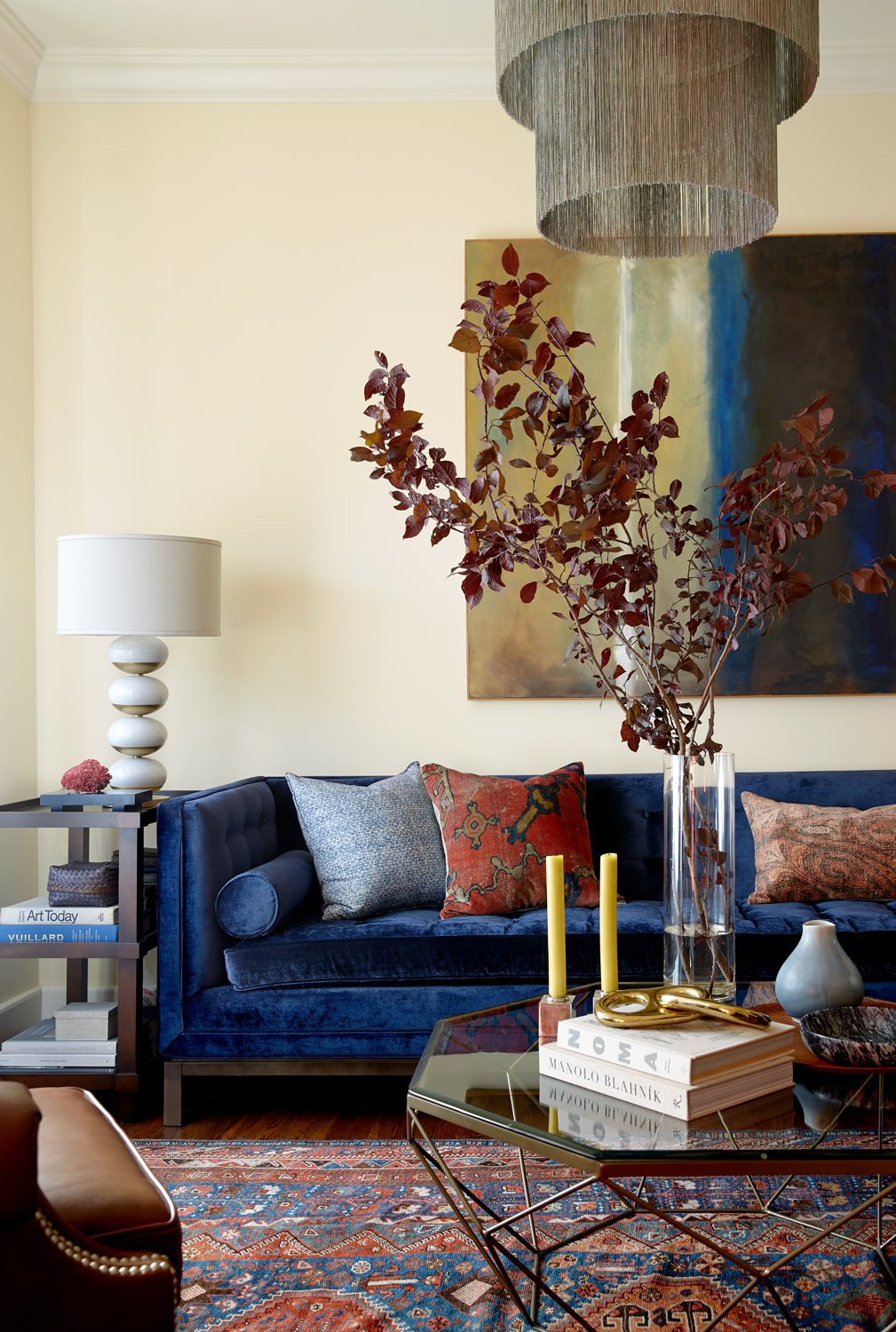Living room with a blue velvet sofa, a sculptural table lamp, layered abstract artwork, and a patterned rug