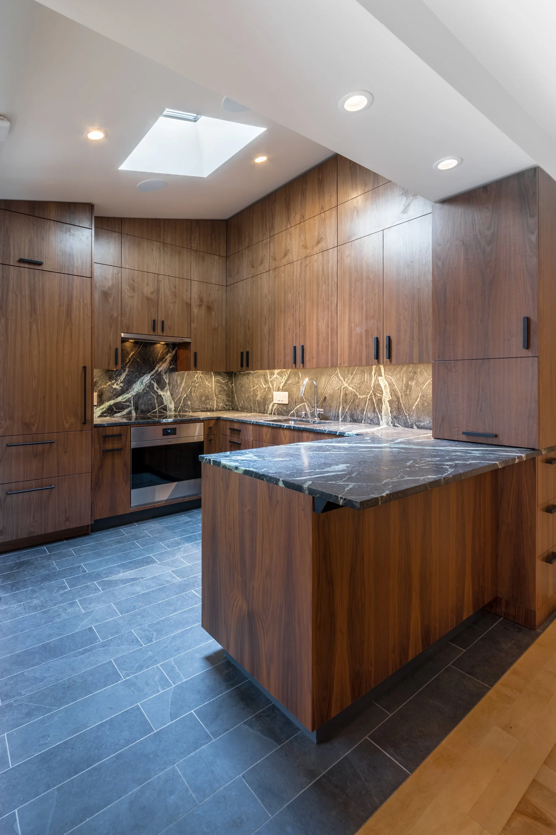 Custom walnut cabinetry and a marble-topped peninsula beneath a skylight in the remodeled Mission District kitchen
