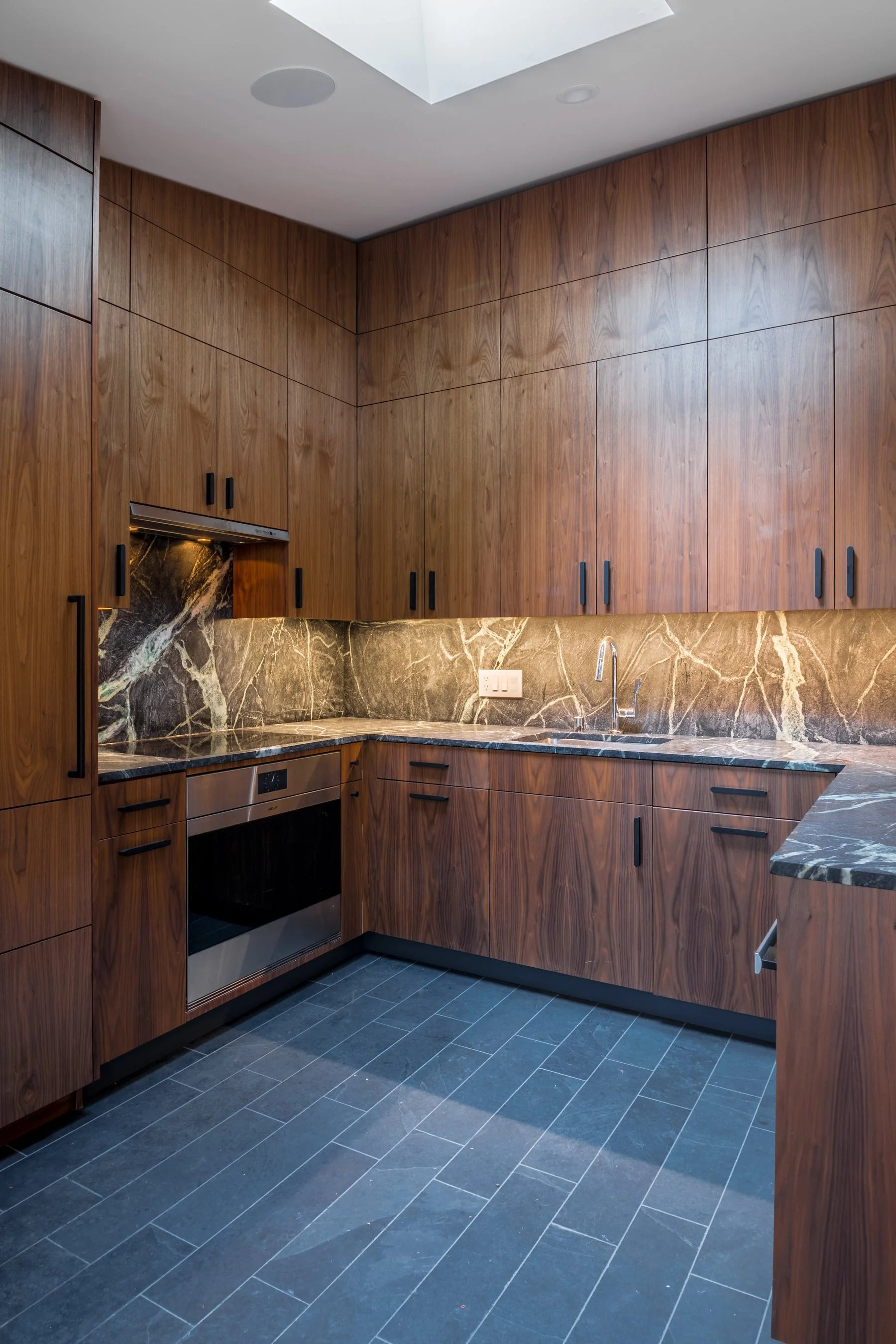 Floor-to-ceiling walnut cabinetry and the sink wall lit by a skylight in the remodeled kitchen