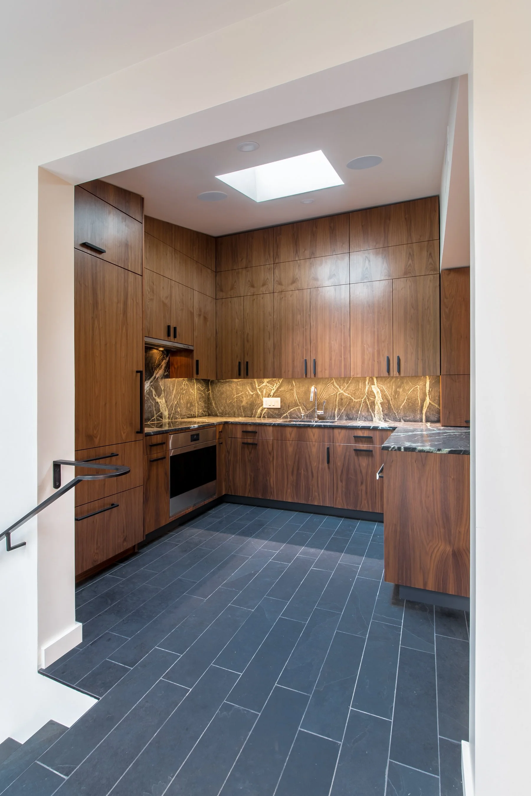 View into the remodeled kitchen from the stair landing, showing walnut cabinetry and slate tile floors