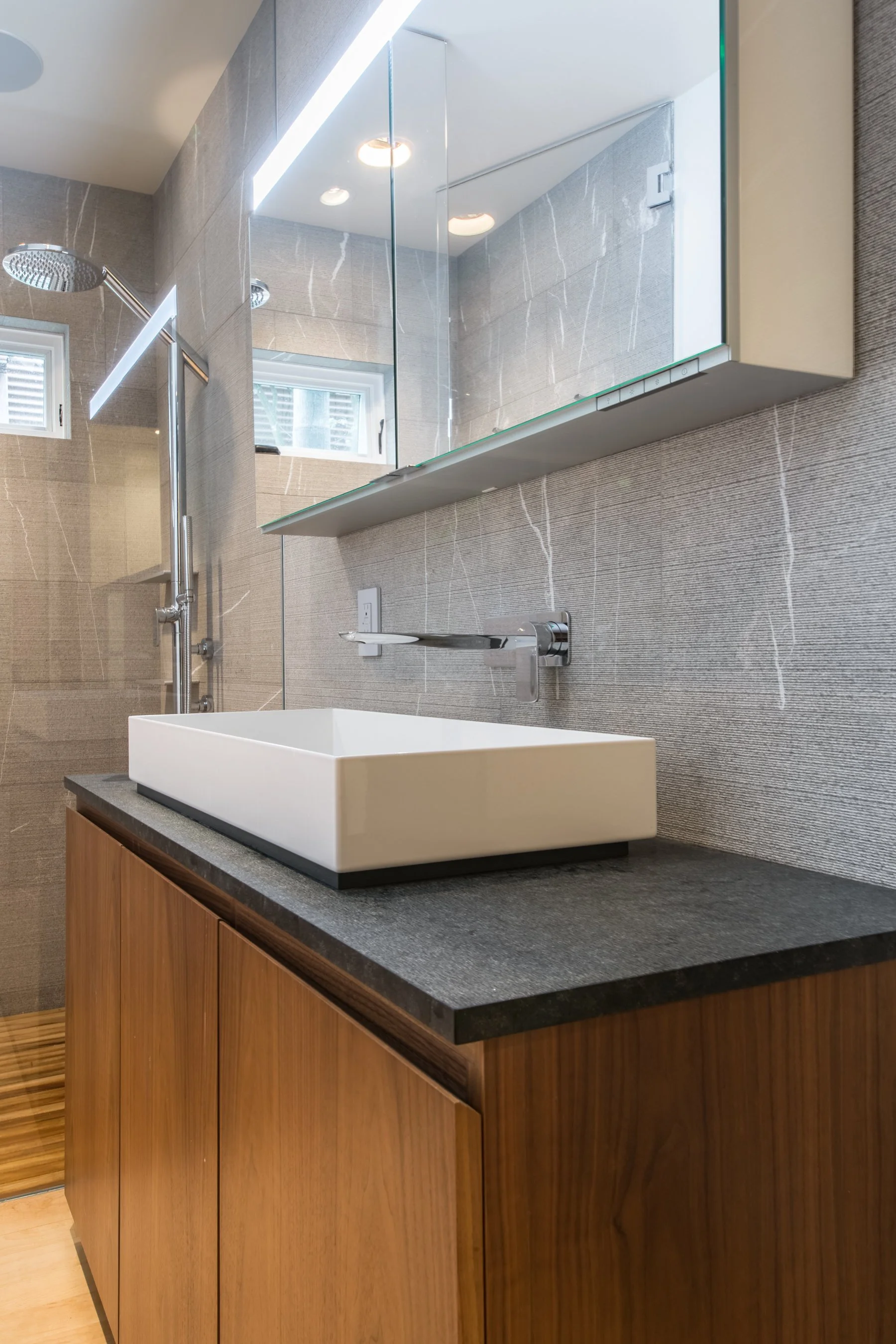 Close view of the rectangular vessel sink, honed black stone counter and chrome wall-mounted faucet