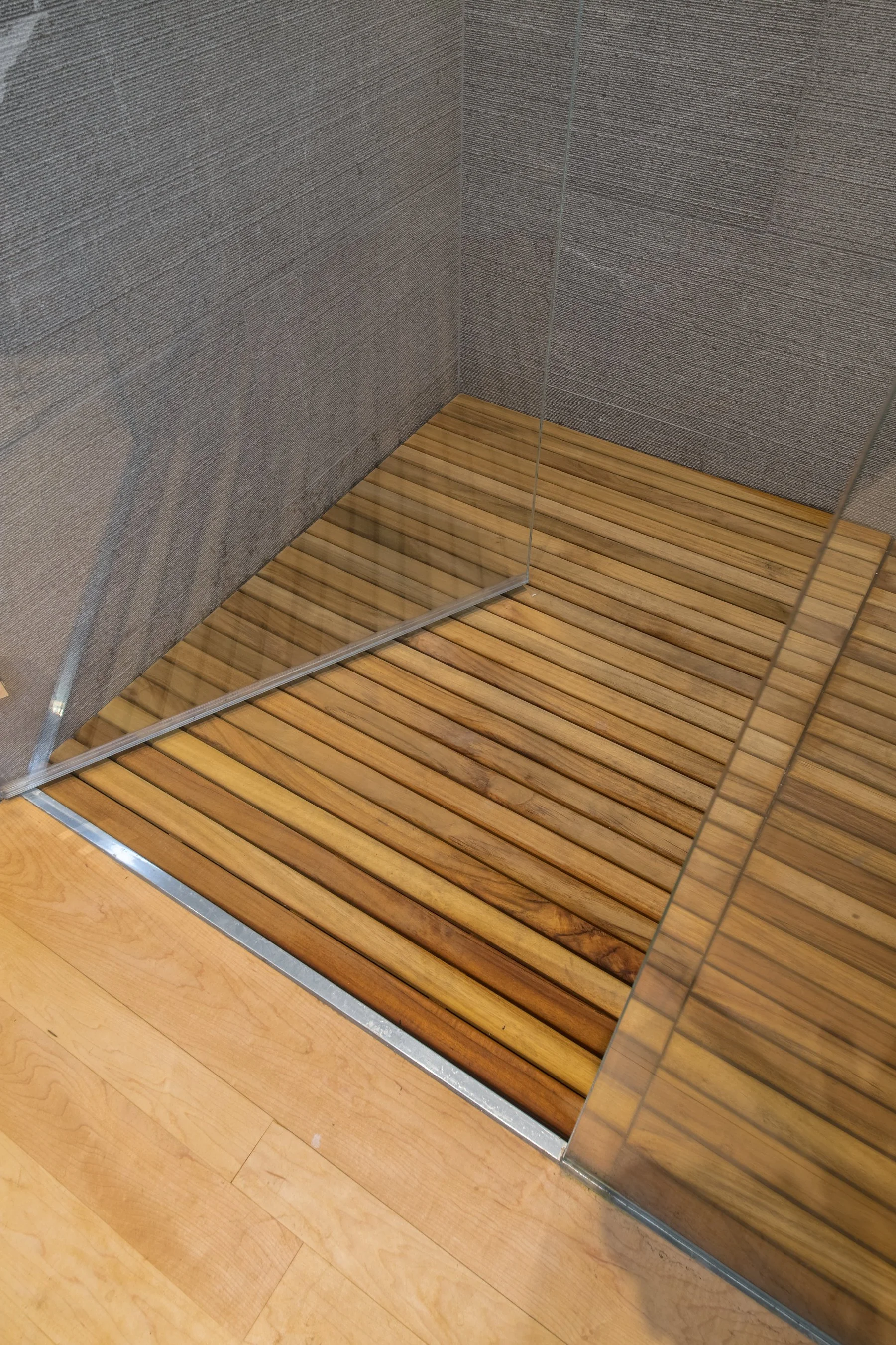 Teak slat shower floor set flush with the maple hardwood at the glass shower threshold