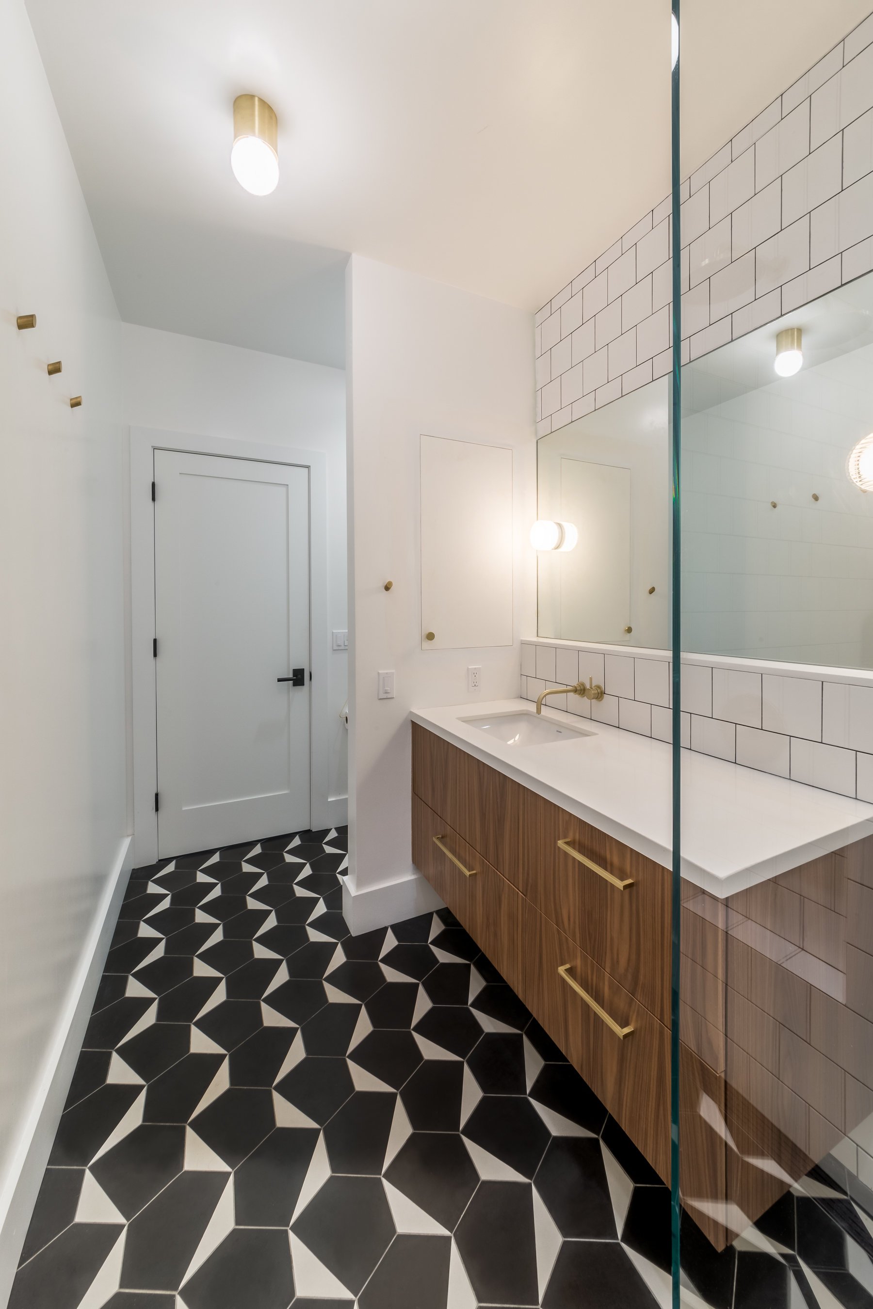 Wide view of the guest bathroom, black-and-white cement floor tile running to a white panelled door