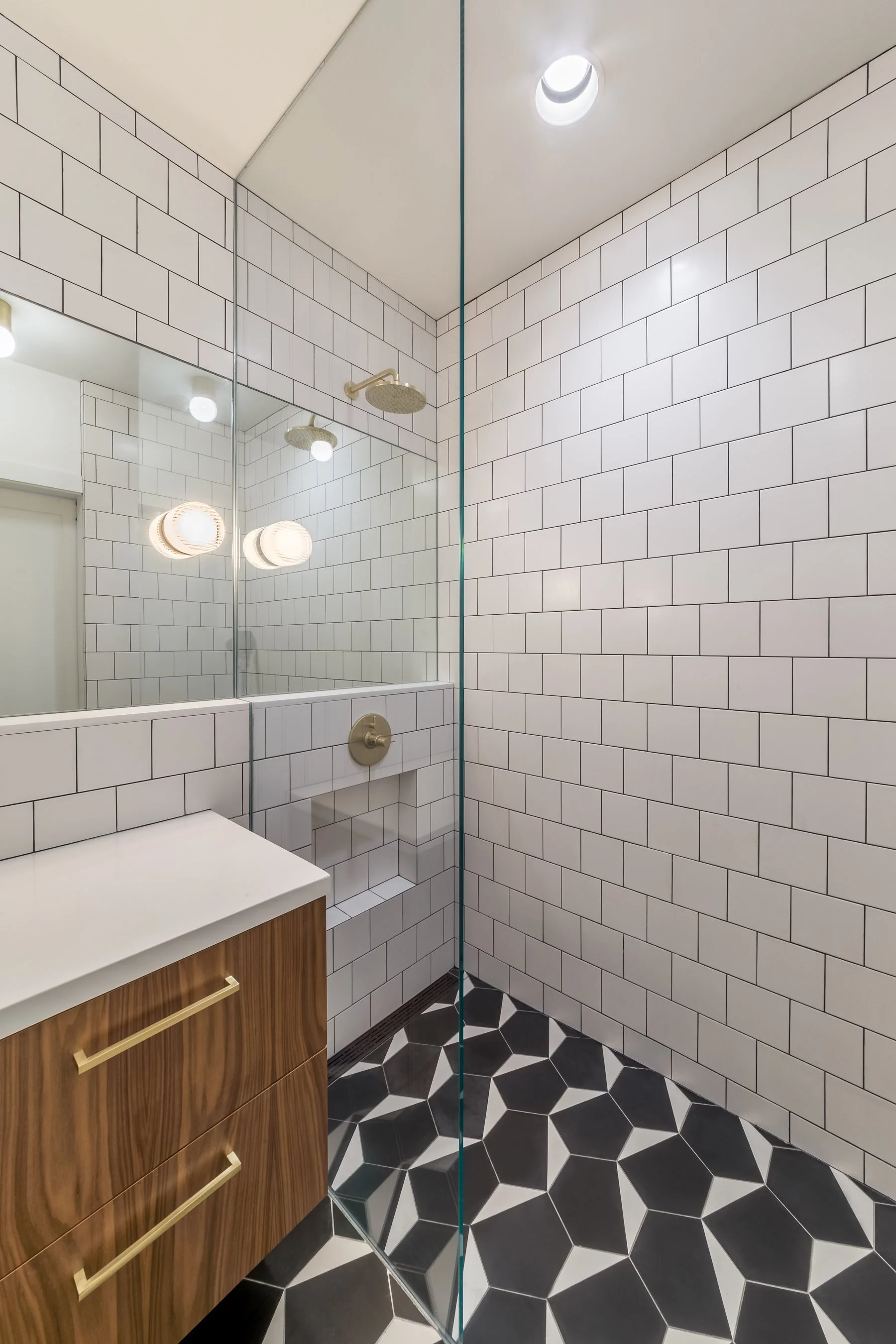 Walk-in shower with brass rain head, tiled bench and full-height white square tile behind clear glass