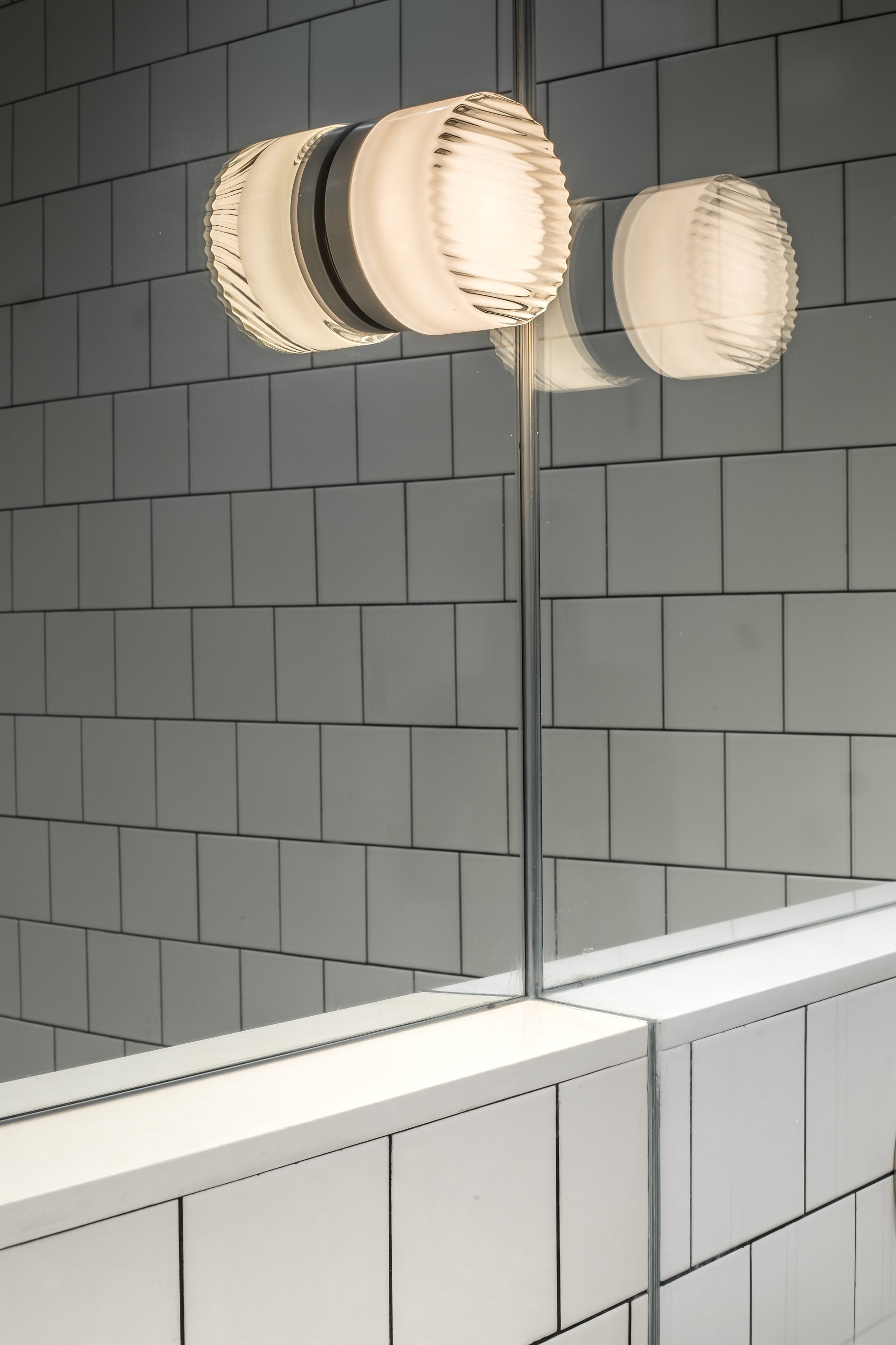Detail of the ribbed glass sconce reflected in the mirror above the shower glass