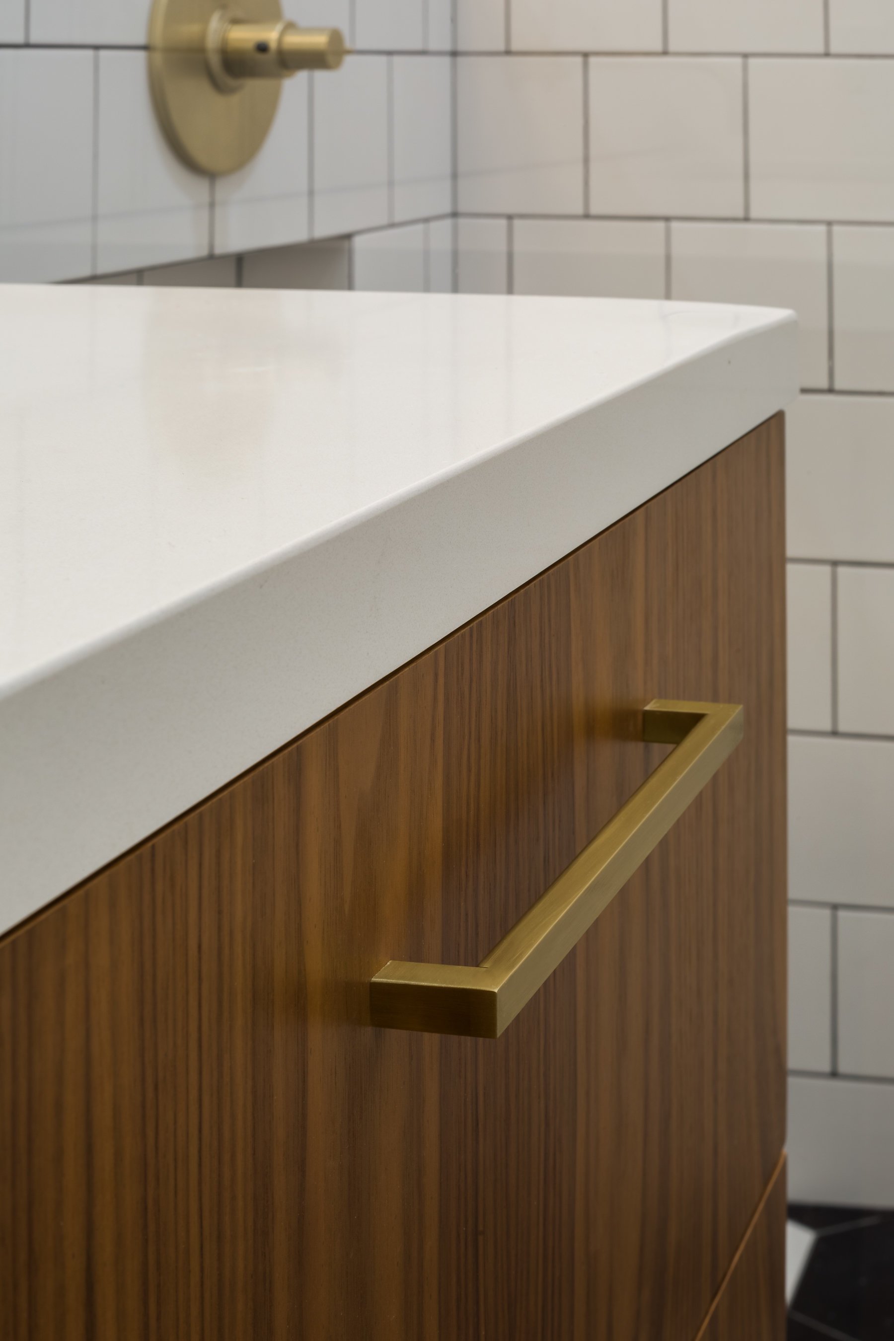 Detail of the white quartz countertop meeting walnut drawer fronts with a brushed brass pull