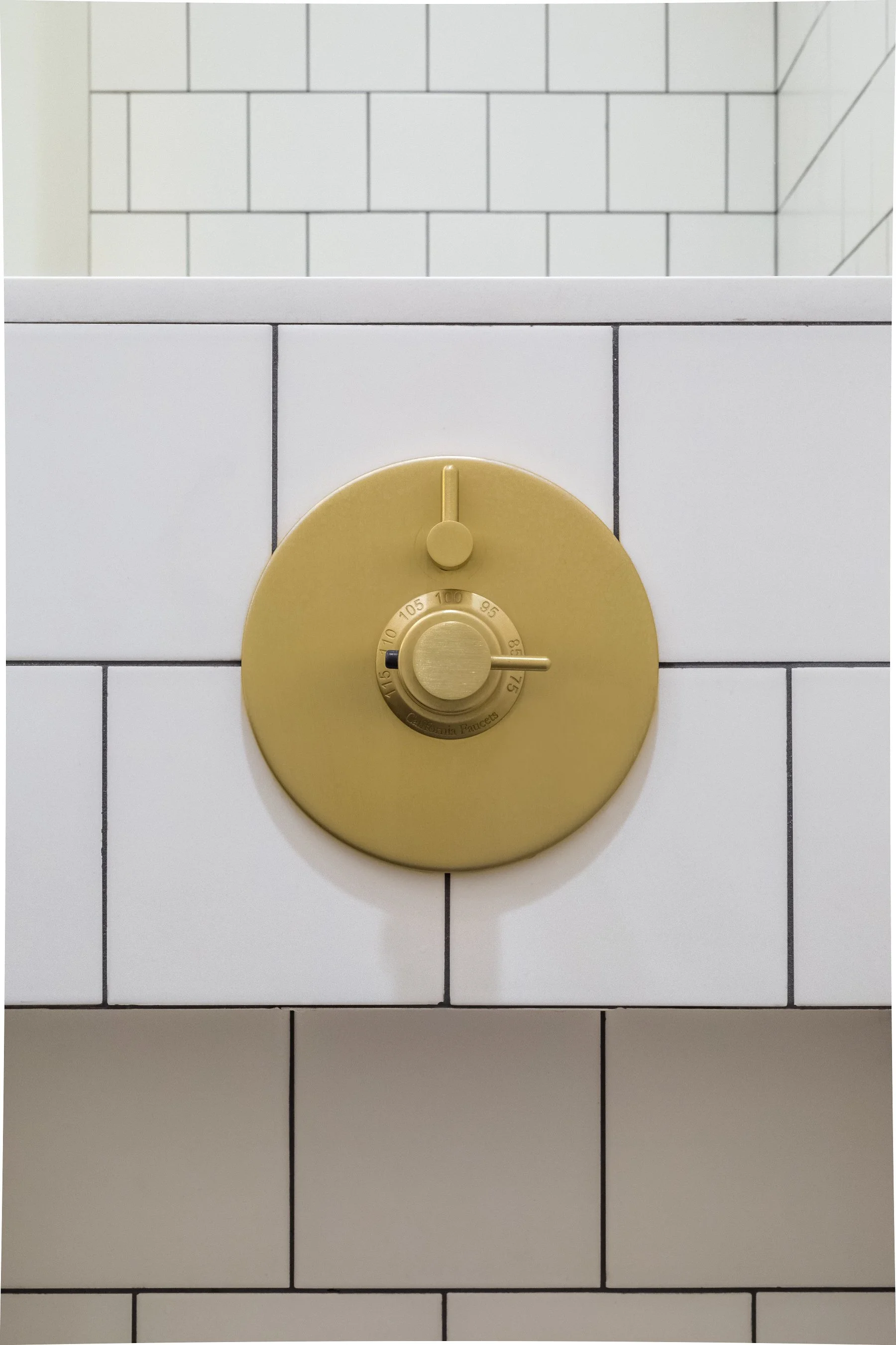 Brushed brass thermostatic shower valve set into the white tiled shower wall