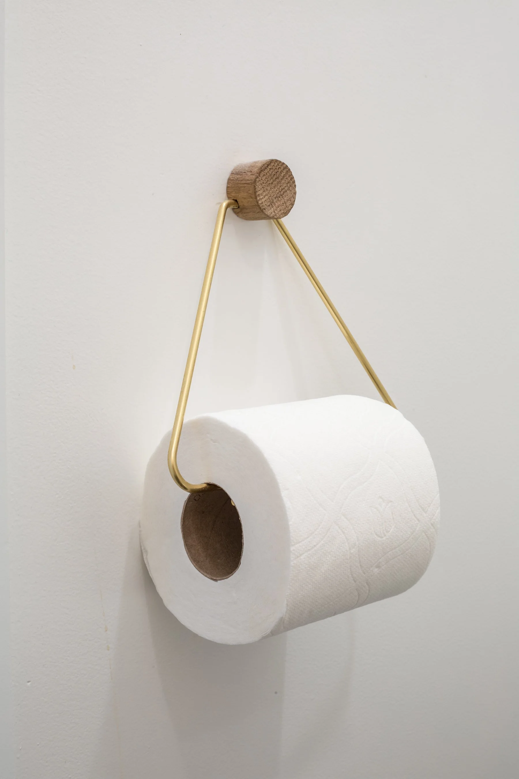 Brass and oak toilet roll holder mounted on the white bathroom wall