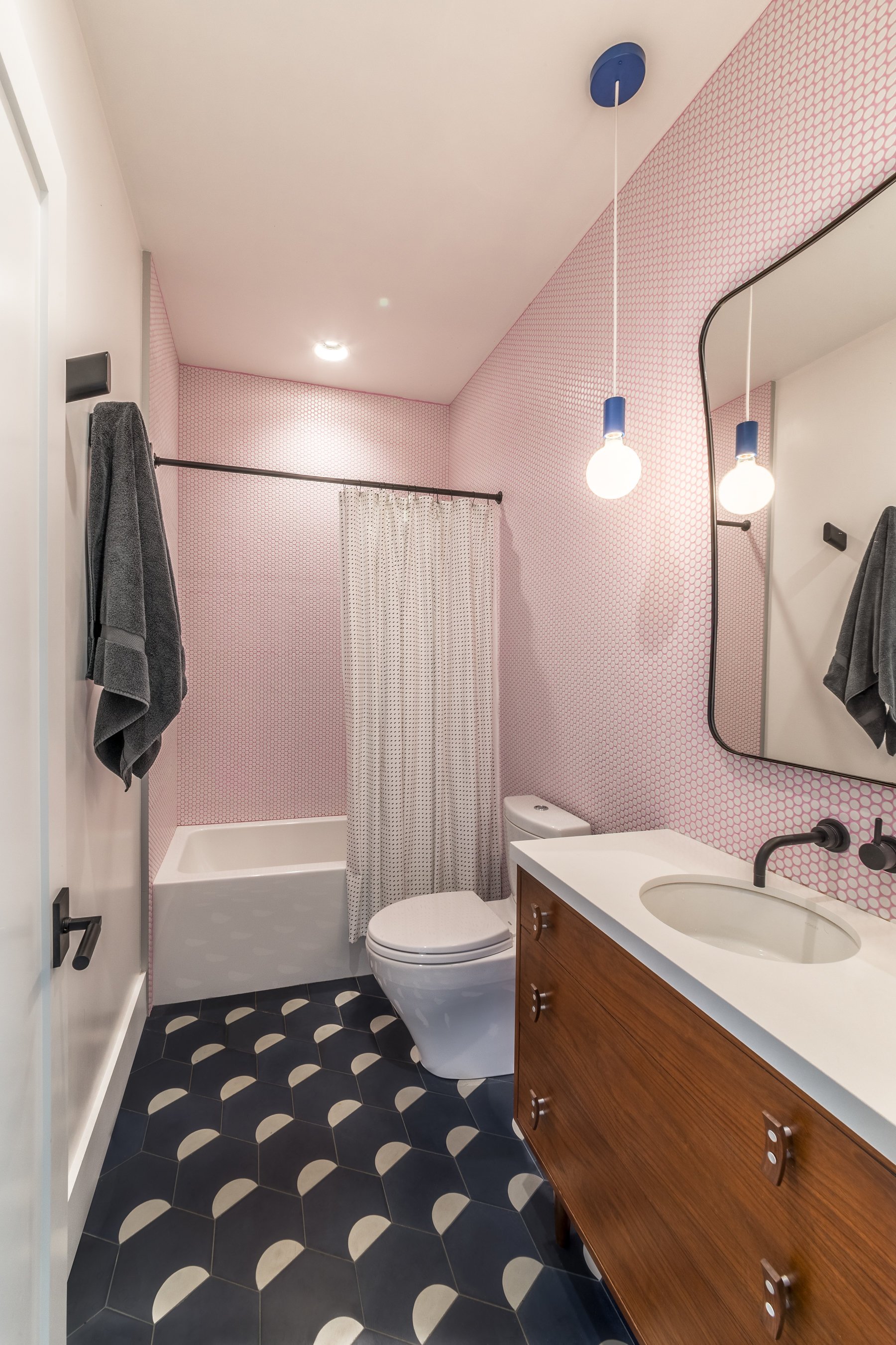 Wide view of the pink penny-tile bathroom showing the tub, shower curtain and navy patterned floor tile