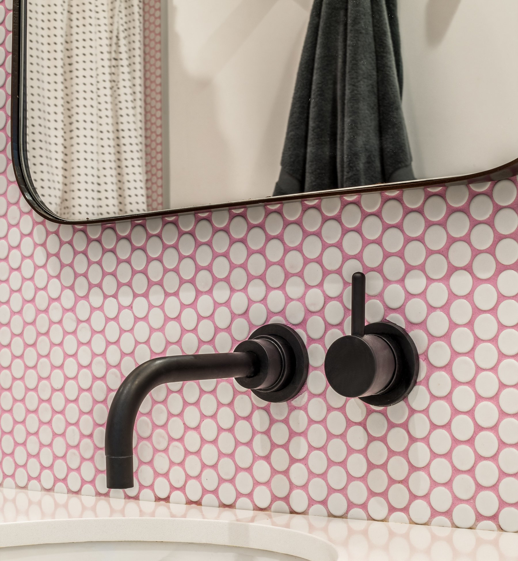 Matte black wall-mounted faucet against the white penny tile set in pink grout