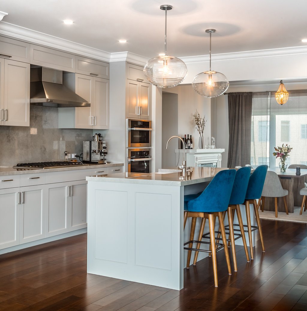 White kitchen with an island, blue bar stools, glass pendants, stainless appliances, and an adjacent living area