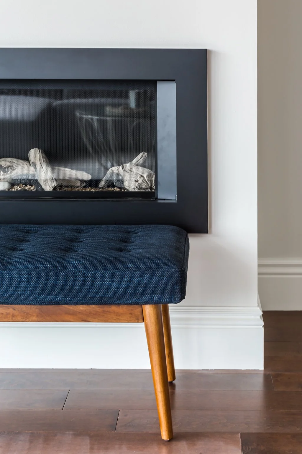 Living area with a black linear fireplace, a navy tufted bench on wood legs, and hardwood floors