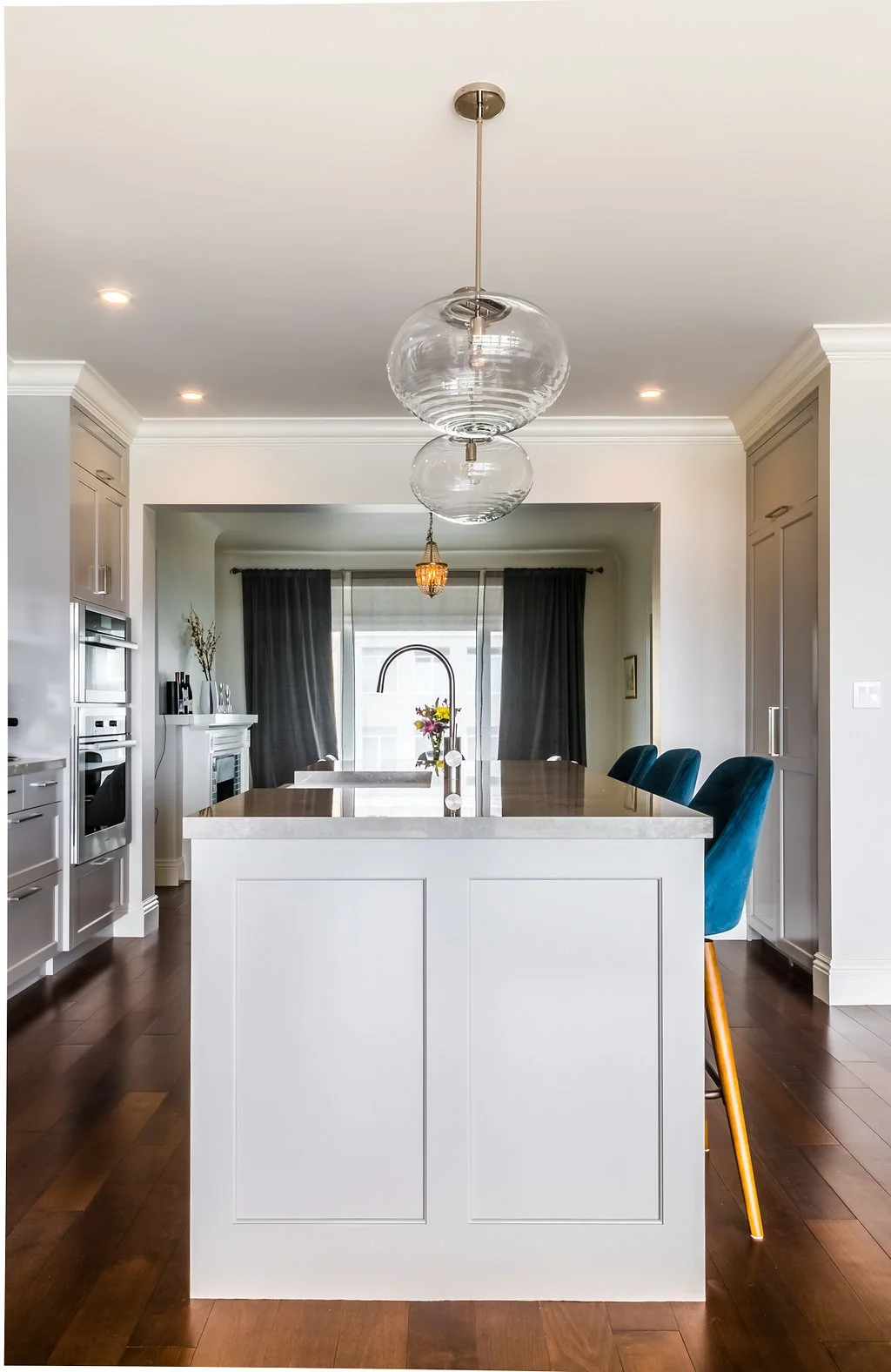 White kitchen with a large island, glass pendant lights, blue bar stools, an arched range niche, and dark hardwood floors