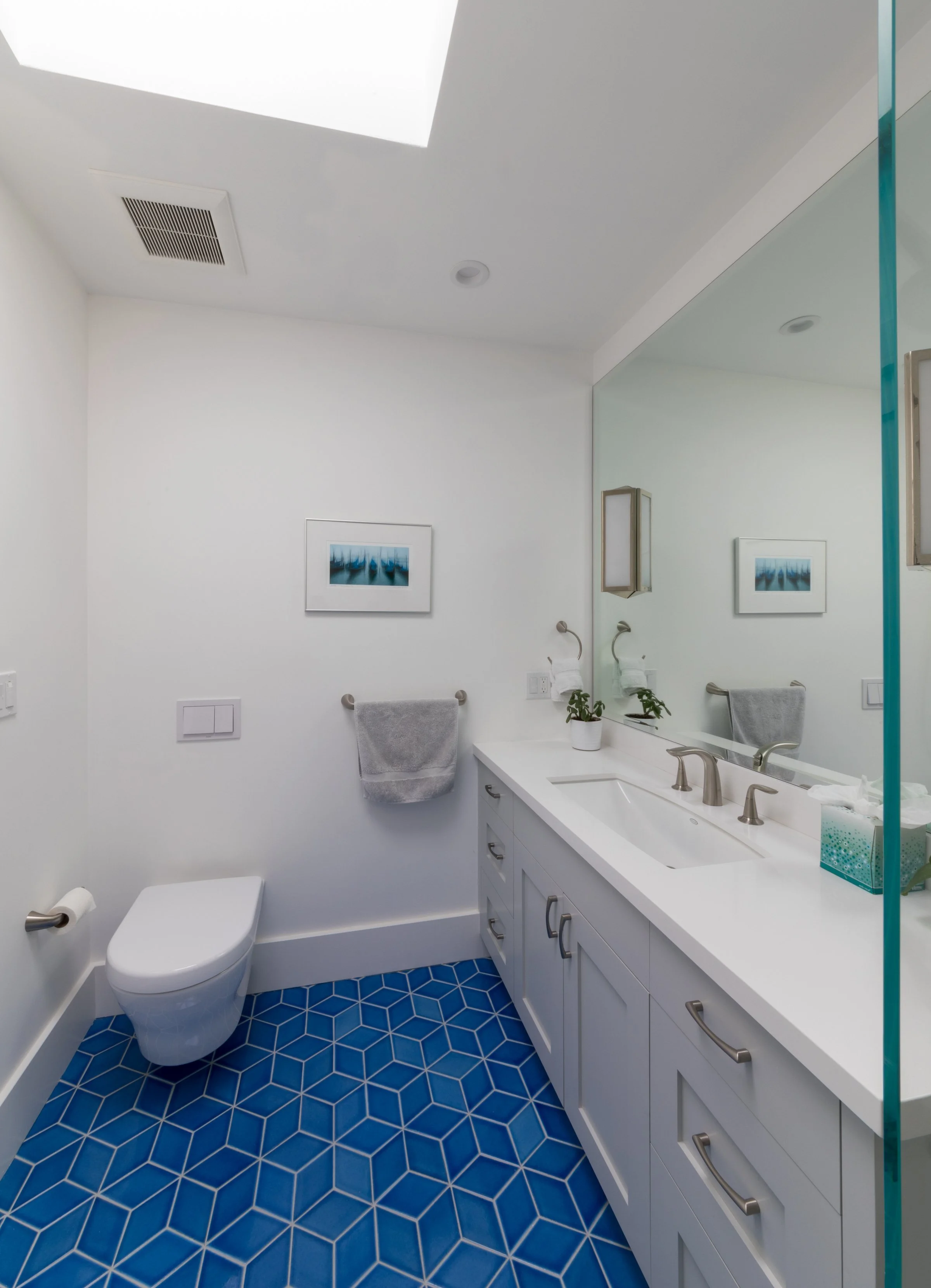 Bathroom with a gray vanity, white counter, a large mirror, blue geometric floor tile, and framed coastal art