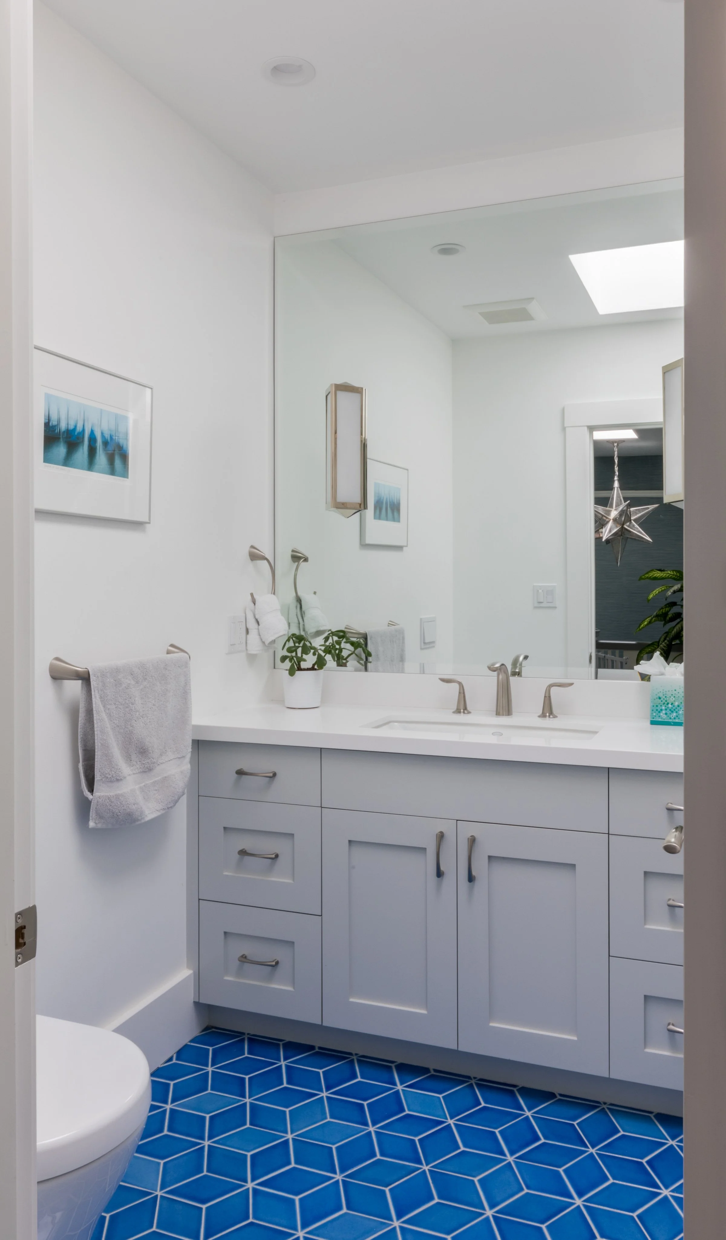 Double-vanity bathroom with gray cabinets, white countertop, a large mirror, and blue diamond-patterned floor tile