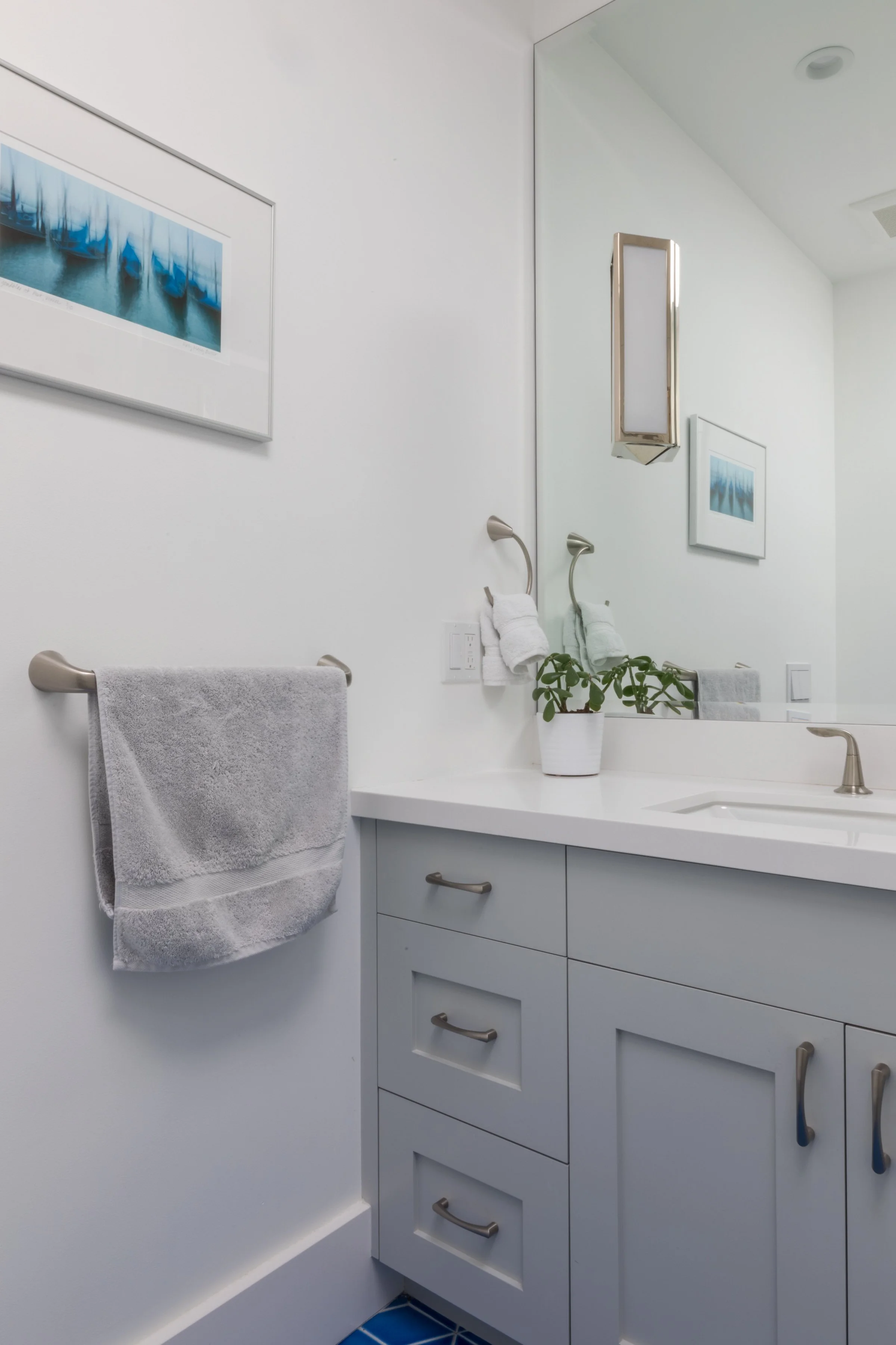 Bathroom vanity with gray cabinets, white counter, a framed blue print, and a gray towel bar