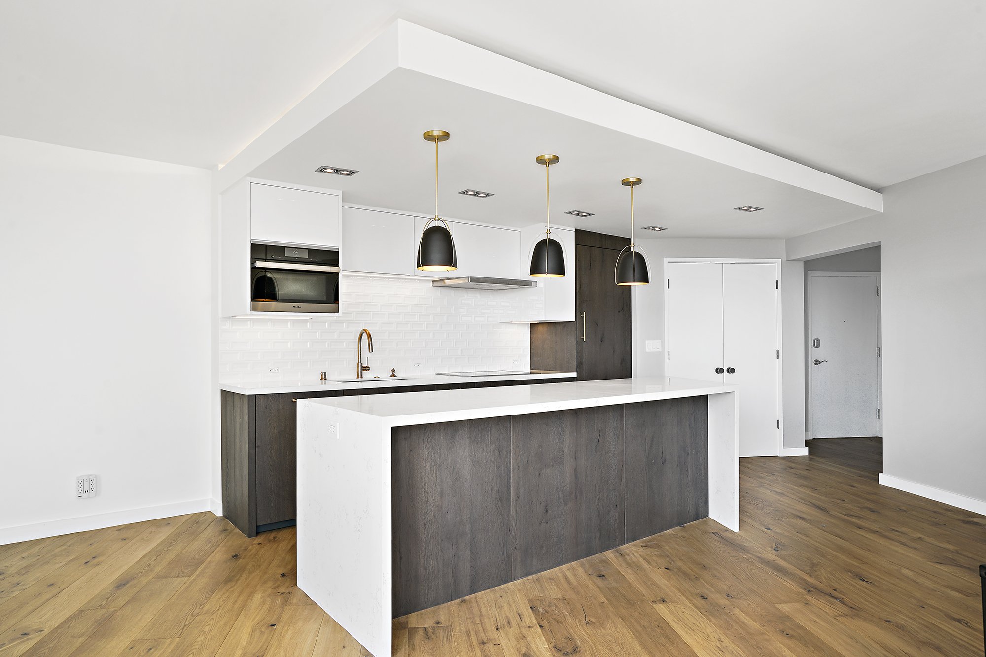Modern white kitchen with a dark wood island, white waterfall countertop, black pendant lights, and light wood floors