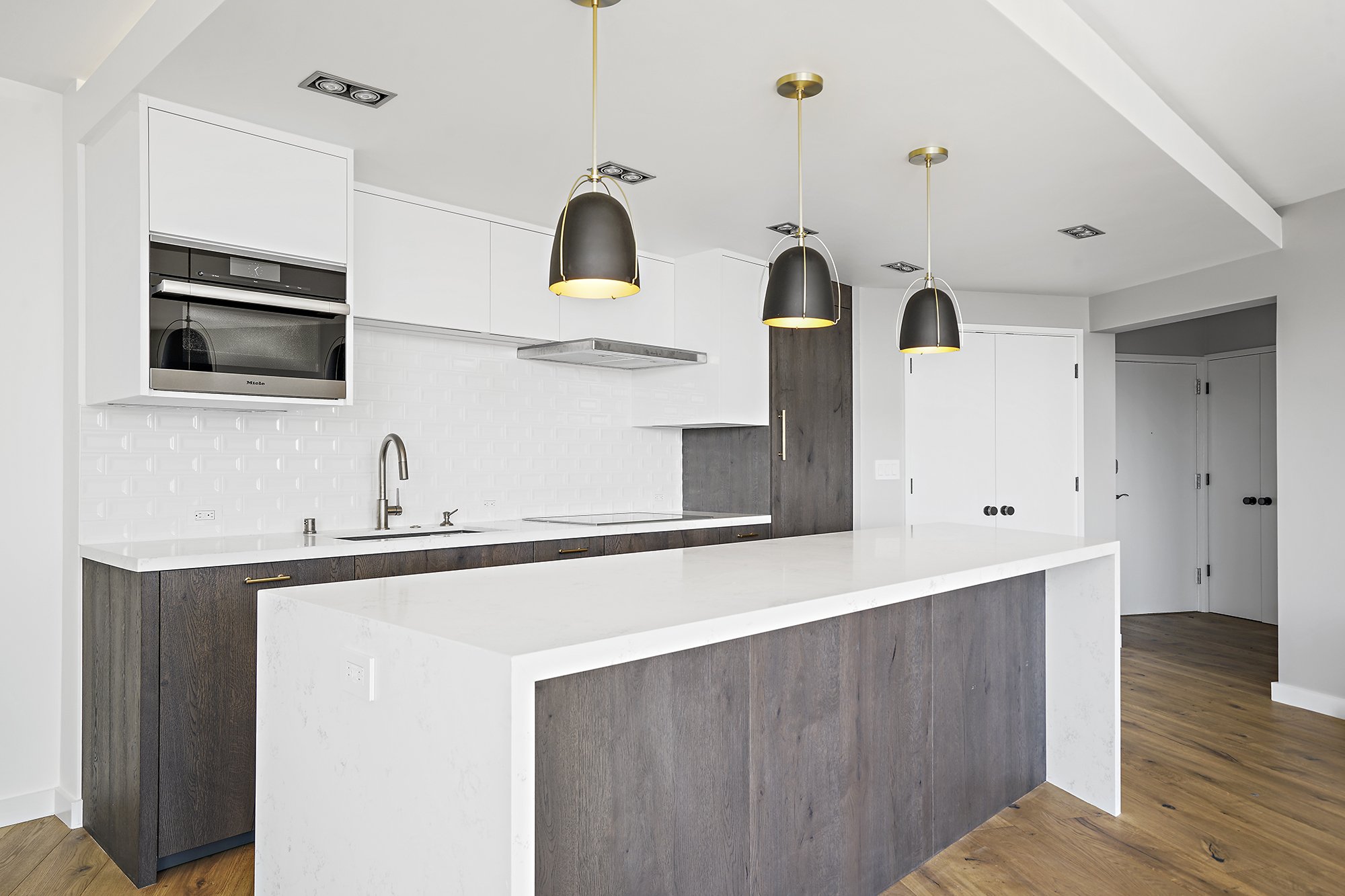 White kitchen with a dark wood island, white quartz counters, white subway-tile backsplash, black pendants, and stainless appliances