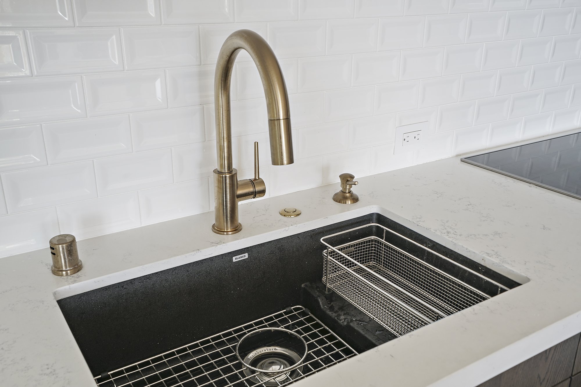 Close-up of an undermount black composite sink with a brass pull-down faucet and a stainless drying basket