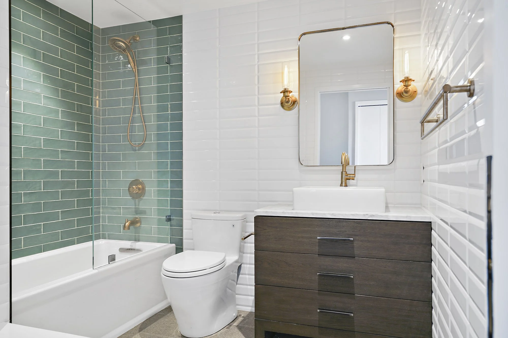 Bathroom with a green glass-tile shower surround, a tub, a dark wood vanity with a vessel sink, brass fixtures, and white subway tile