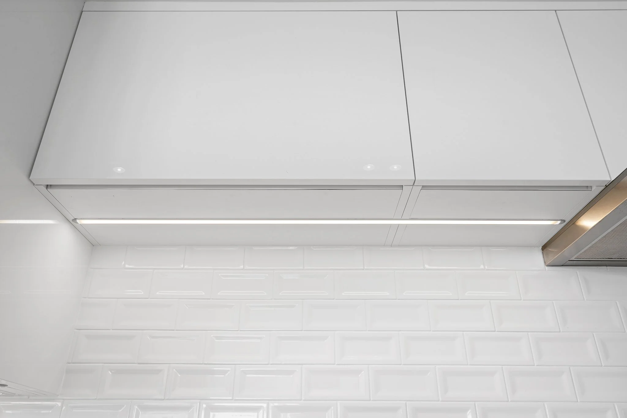 Close-up of a glossy white beveled subway-tile wall with a white cabinet above