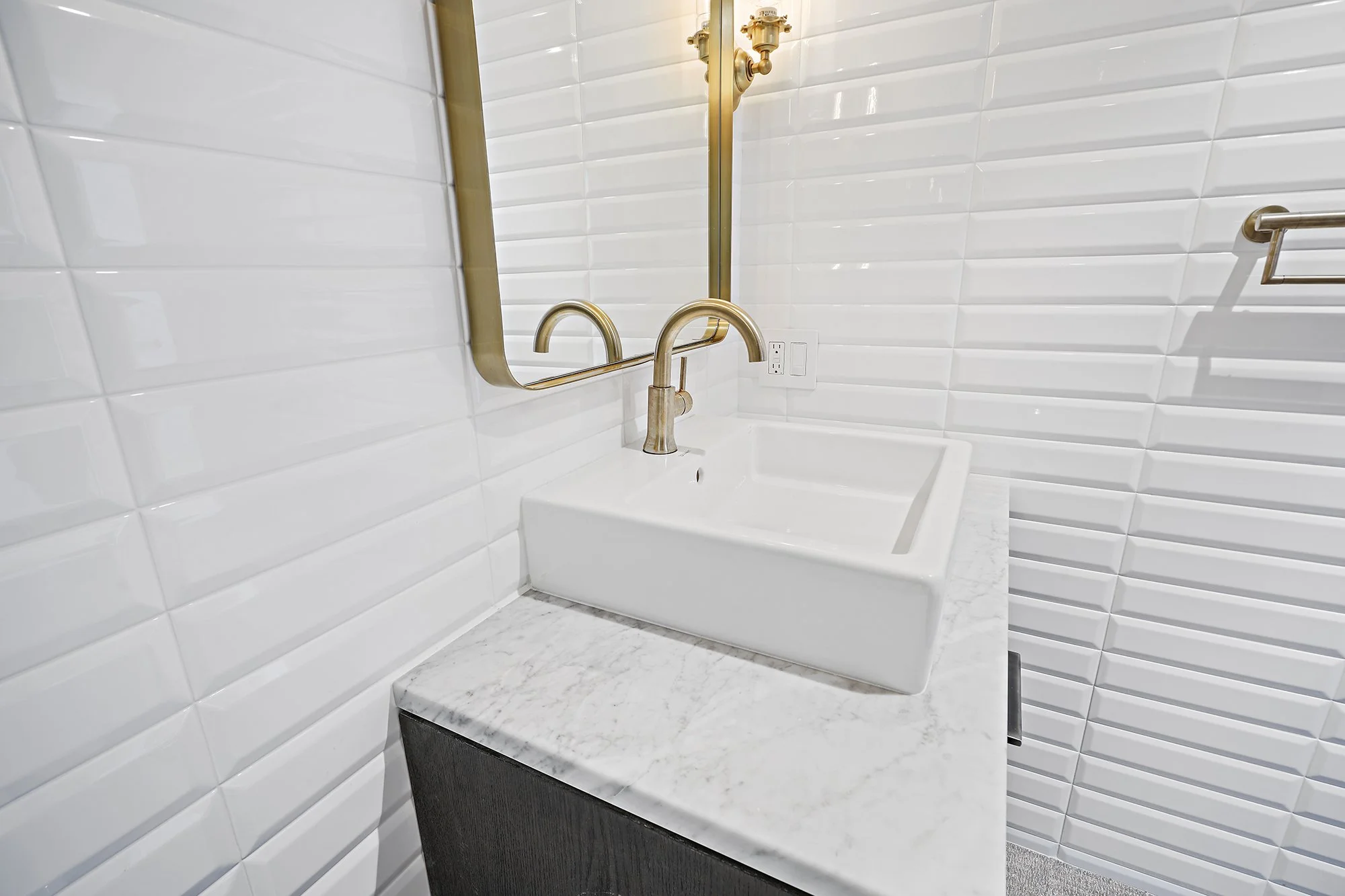 Wall-mounted white vessel sink on a marble ledge with a tall brass faucet against white subway tile