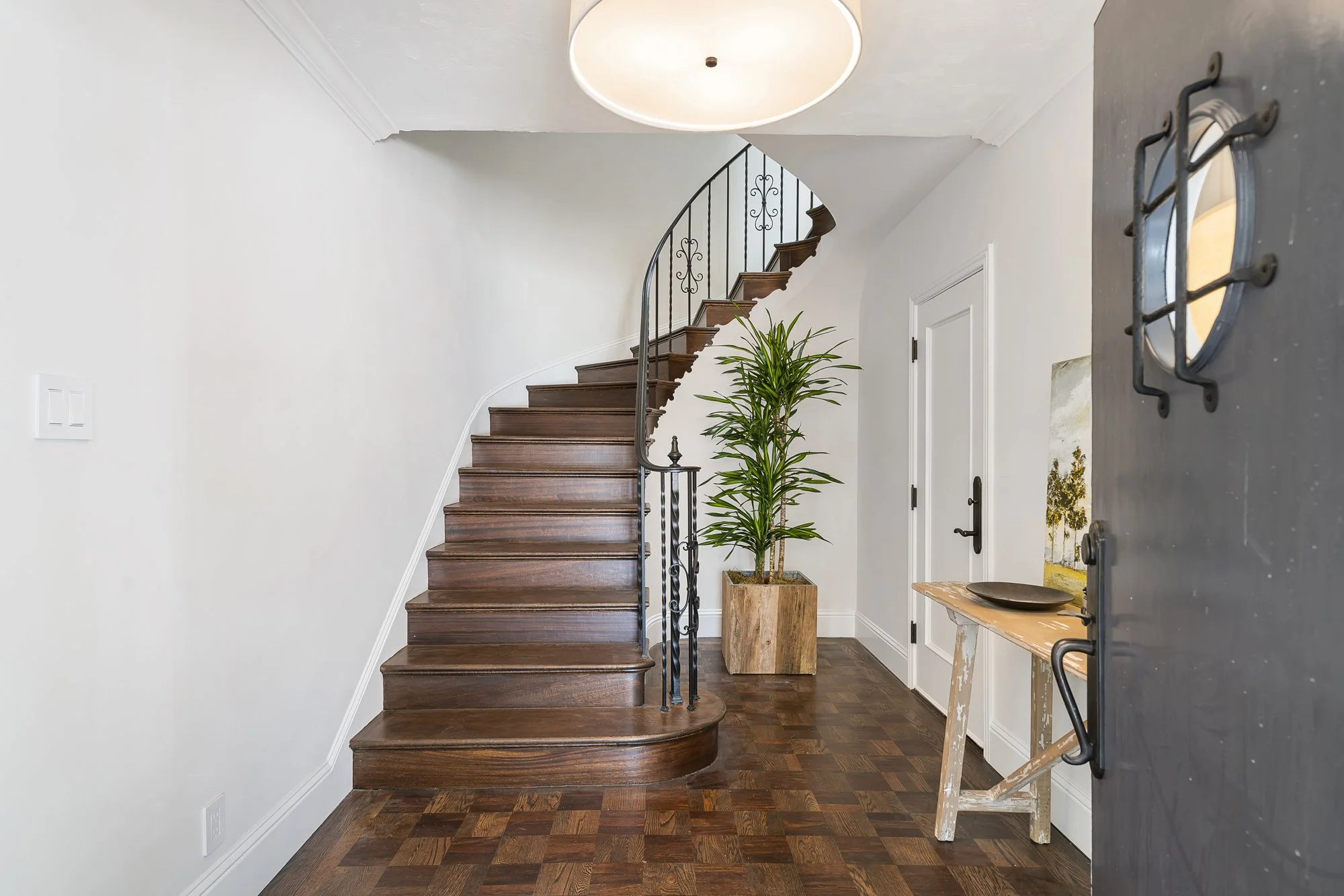 Entry foyer with a curved wood staircase, wrought-iron railing, a nautical wall sconce, and parquet wood floors