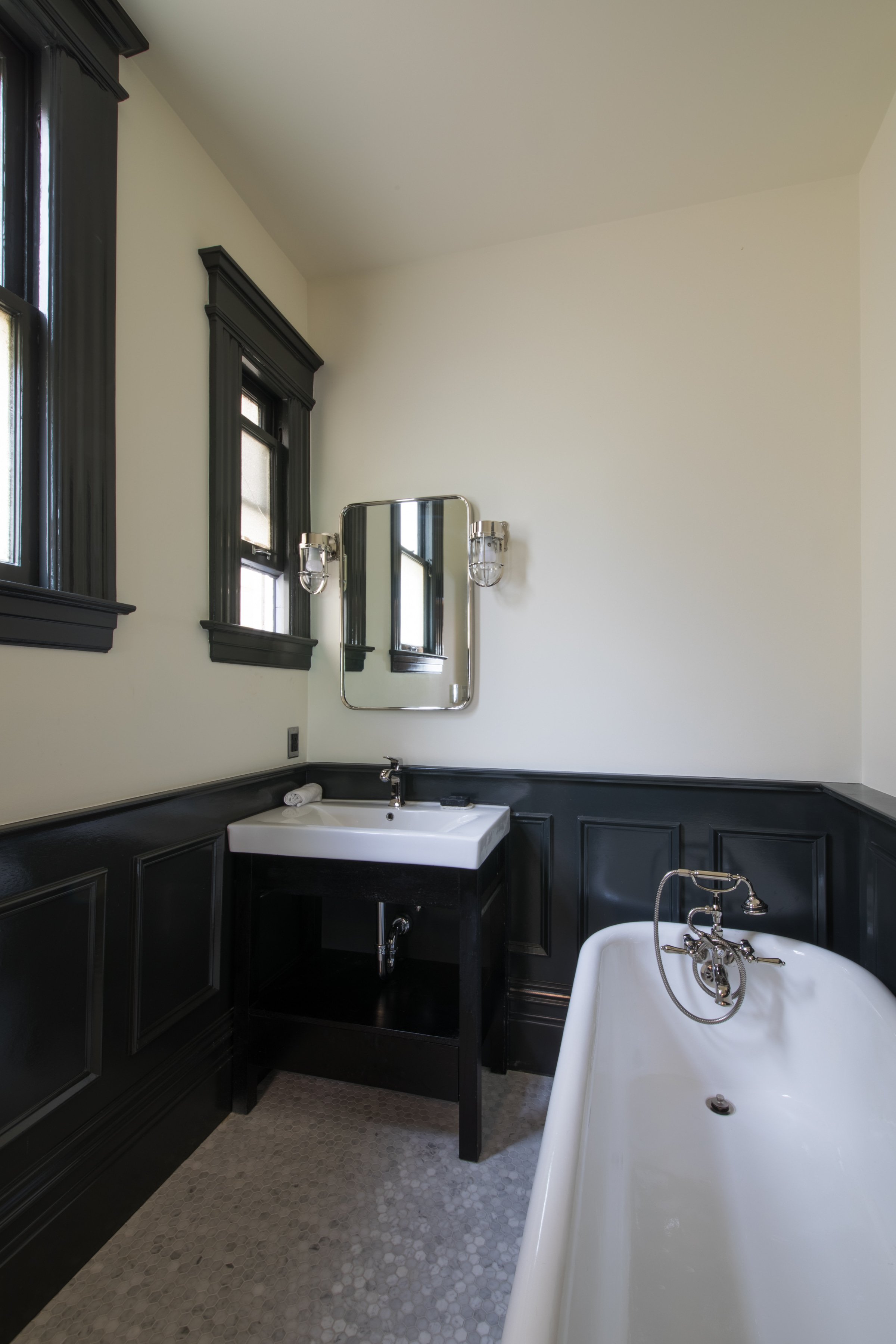 Bathroom with a freestanding tub, black wainscoting, a pedestal sink, and a black-framed window