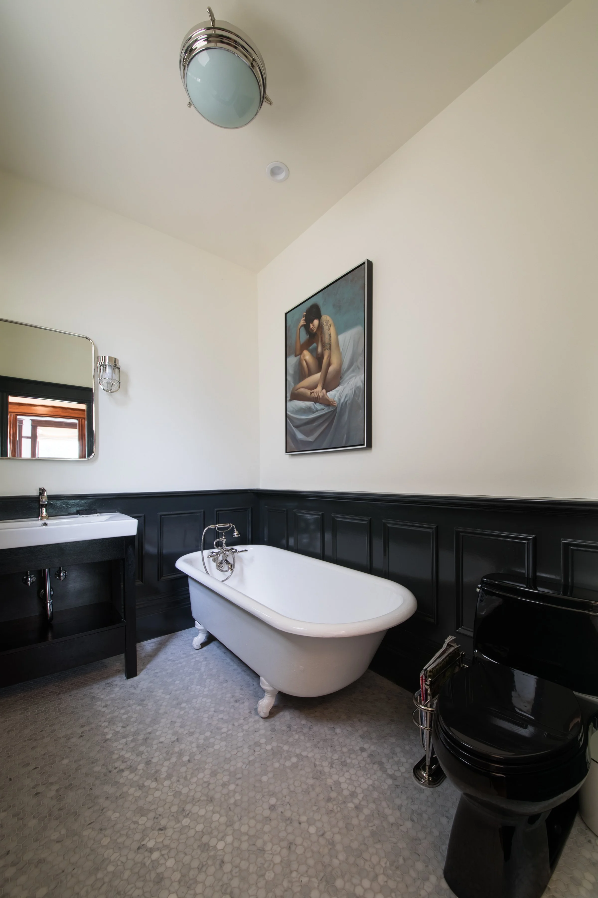 Bathroom with a claw-foot tub, dark wainscoting, a wall sconce, and a terrazzo-style floor