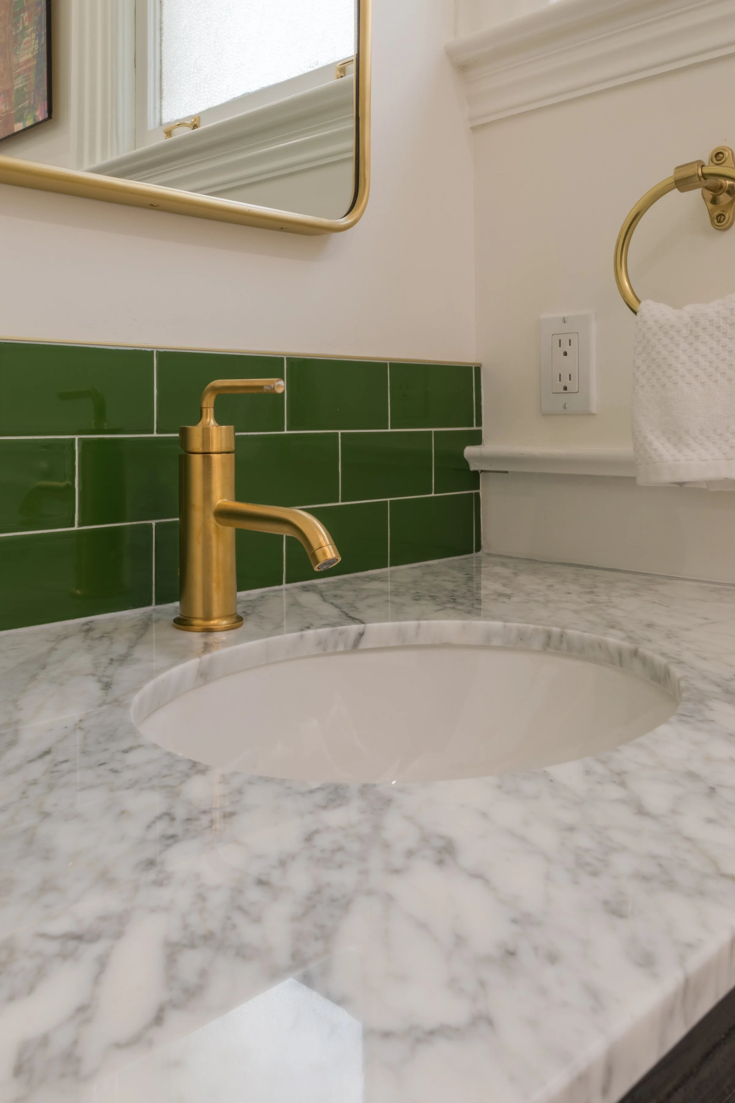 Marble vanity with an undermount sink, brass faucet, green subway-tile backsplash, and a brass towel ring