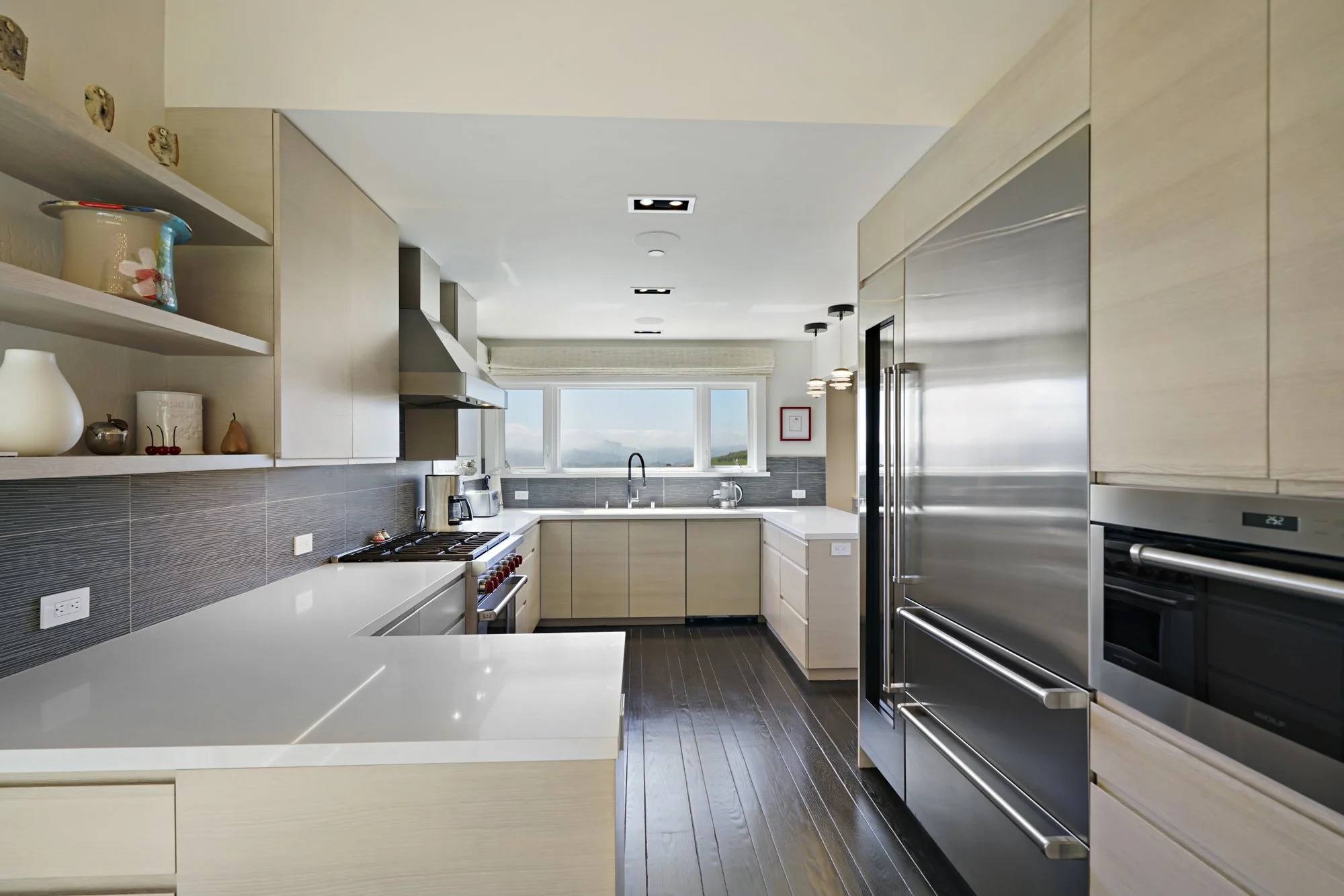 Light wood-toned kitchen with white quartz counters, a gray tile backsplash, stainless appliances, and open shelving