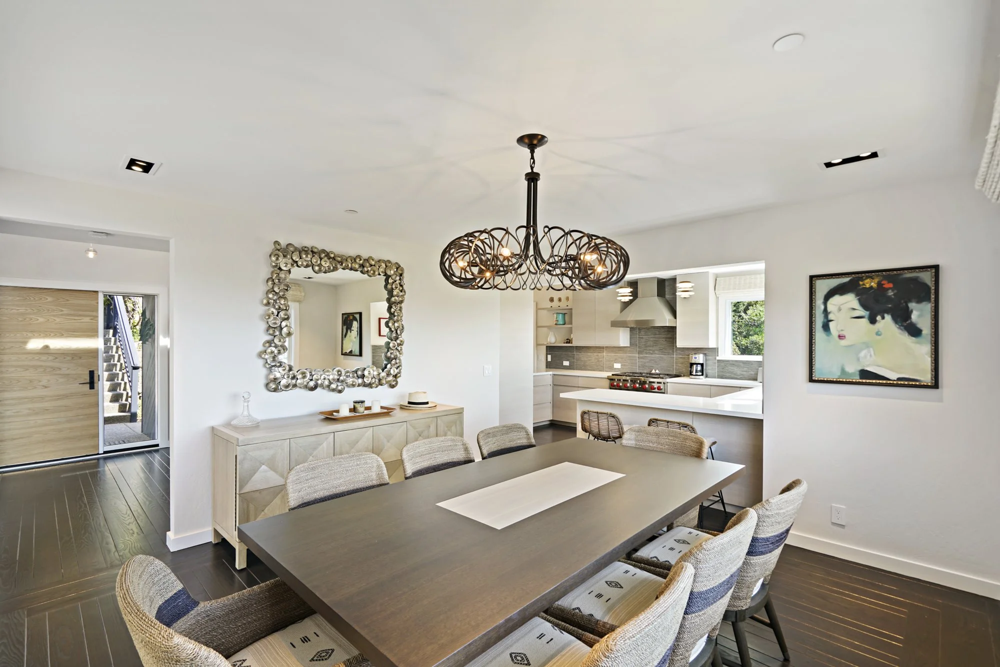Dining area with a wood table, woven-back chairs, a spherical pendant light, ornate mirrors, and hardwood floors