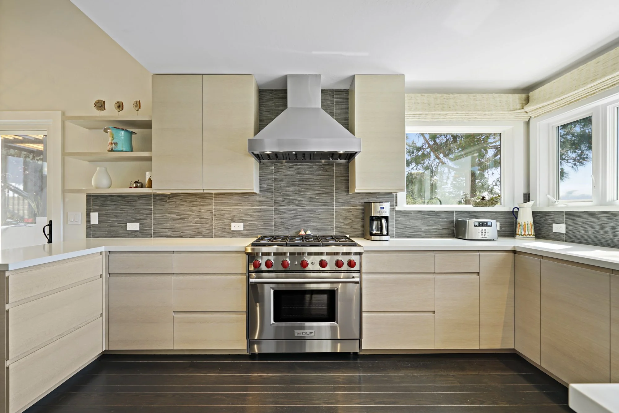 Light wood kitchen with a stainless gas range, stainless hood, gray tile backsplash, and corner windows