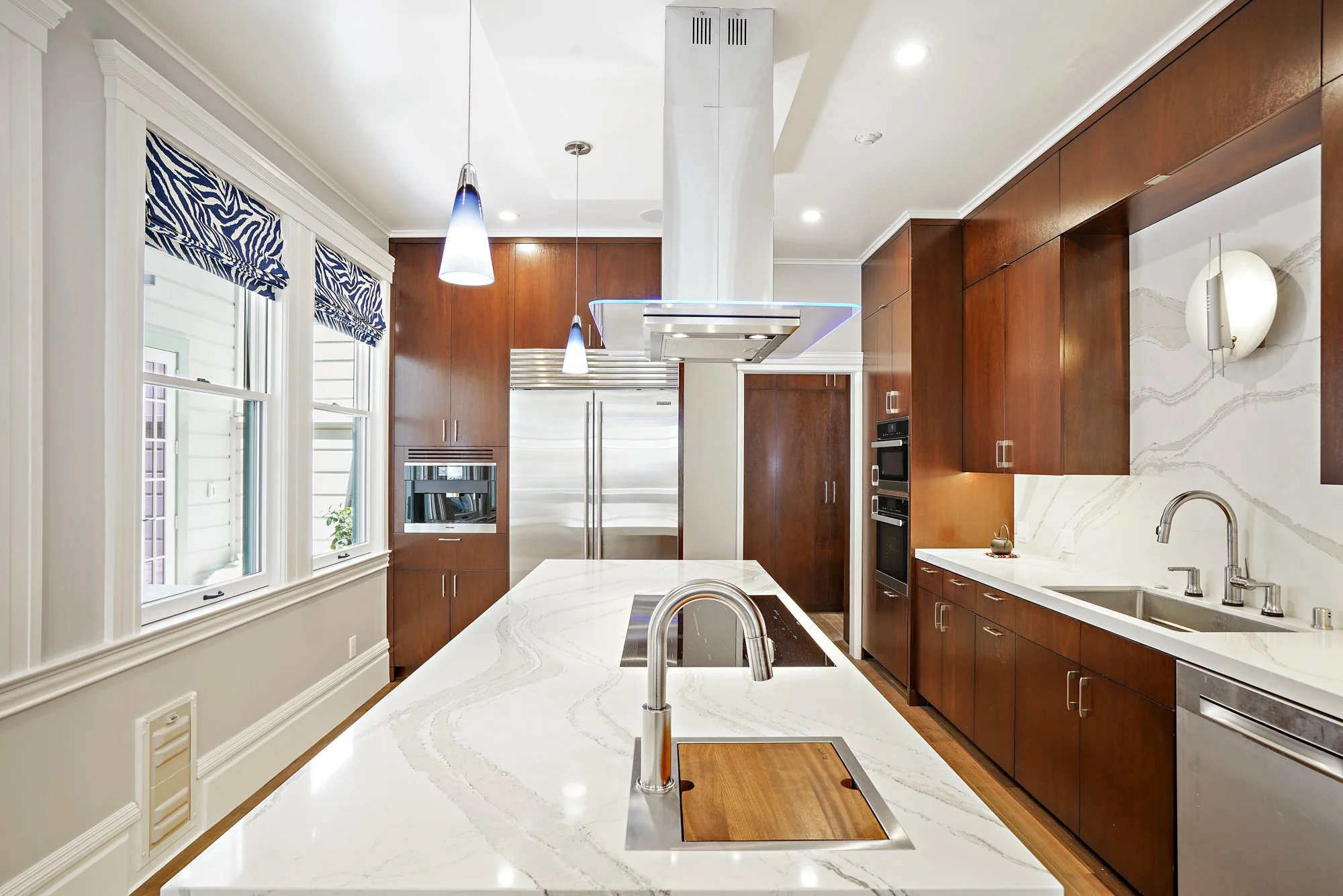 Wood kitchen with a large marble island and wood-inset sink, stainless appliances, and windows with patterned valances